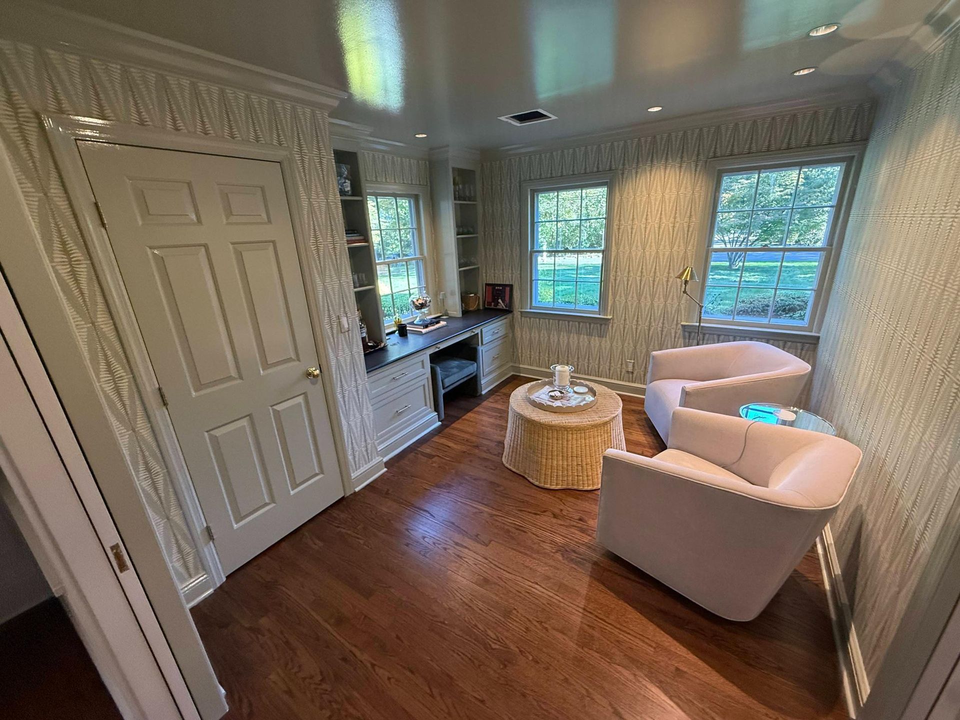 Bright sunroom with white chairs, round wicker table, wood floors, and large windows.