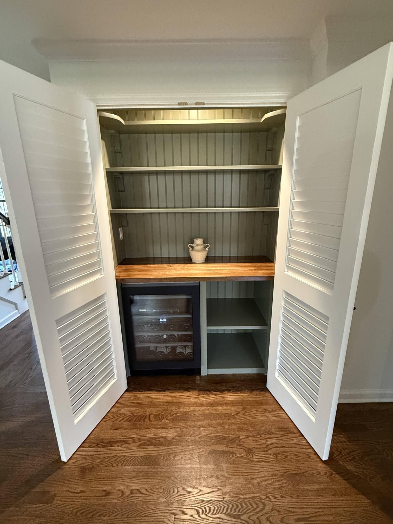 Open pantry cabinets with shelves, countertop, and wine cooler beneath, on a hardwood floor.