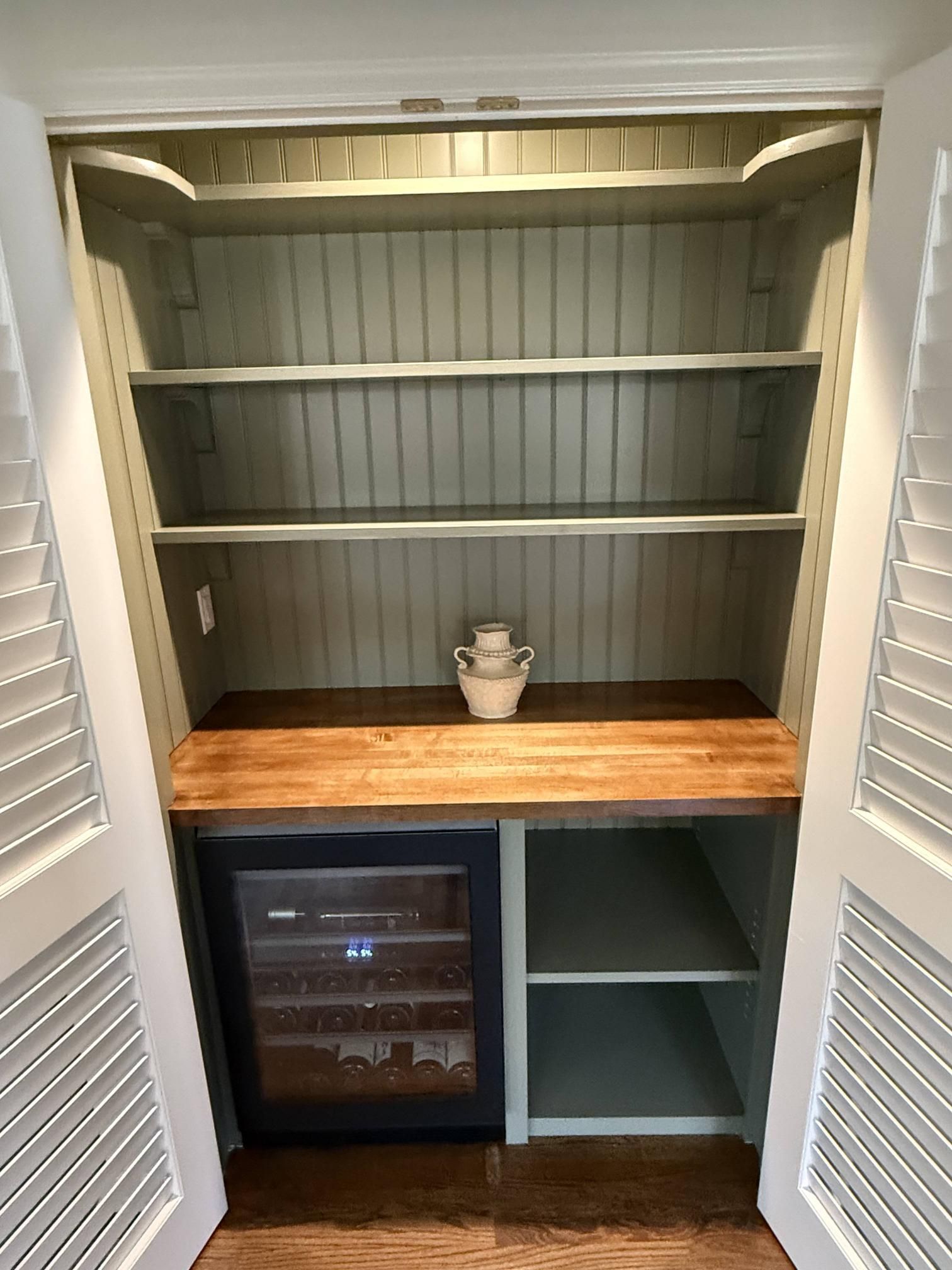 Built-in closet nook with shelves, wood countertop, mini fridge, and a small potted plant