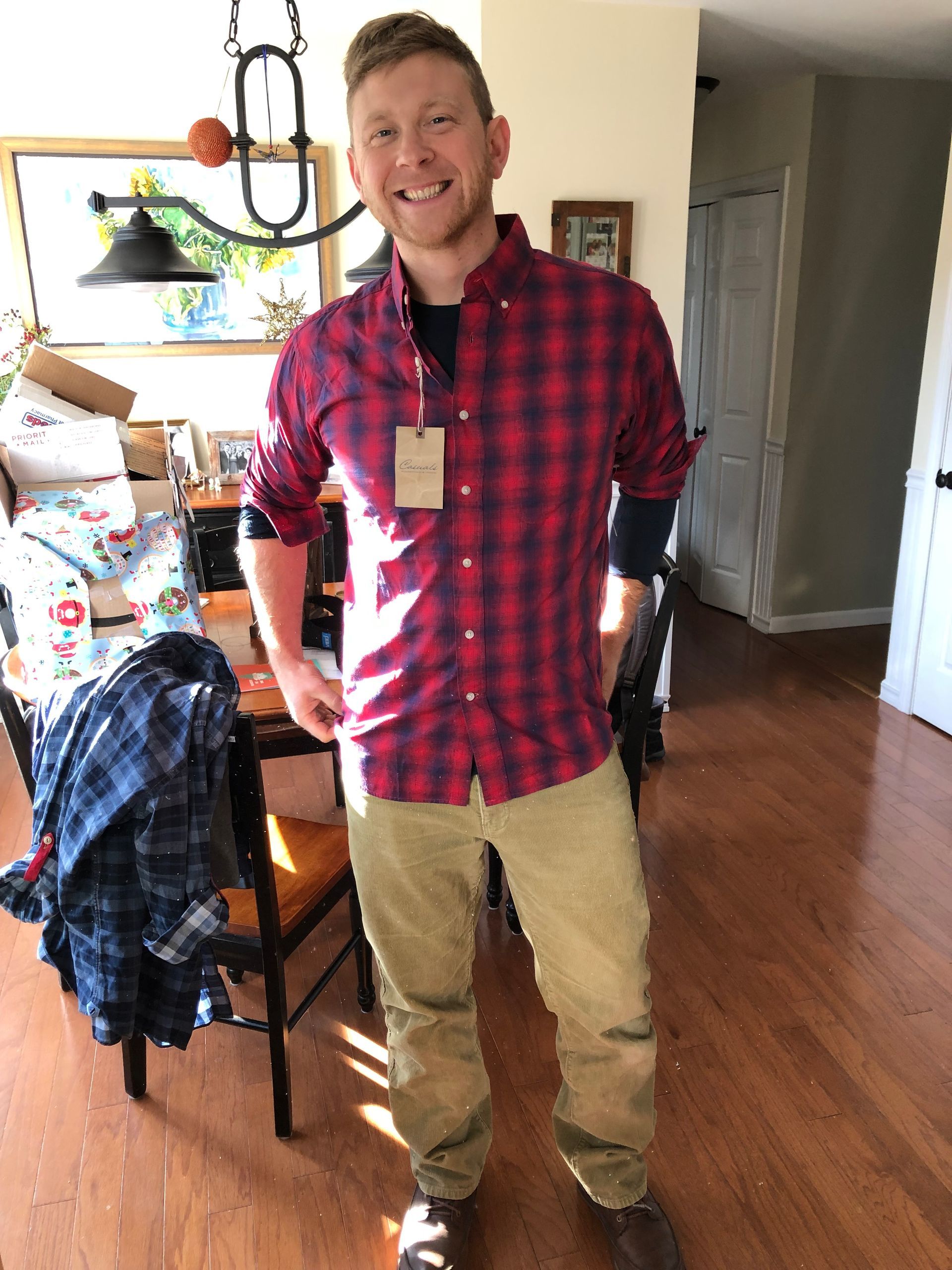 Smiling man in red plaid shirt and tan pants standing in a kitchen-dining room