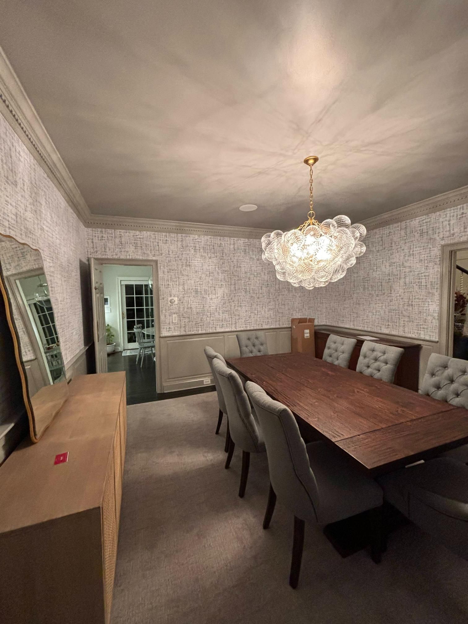 Elegant dining room with long wood table, tufted bench, chandelier, and textured gray walls