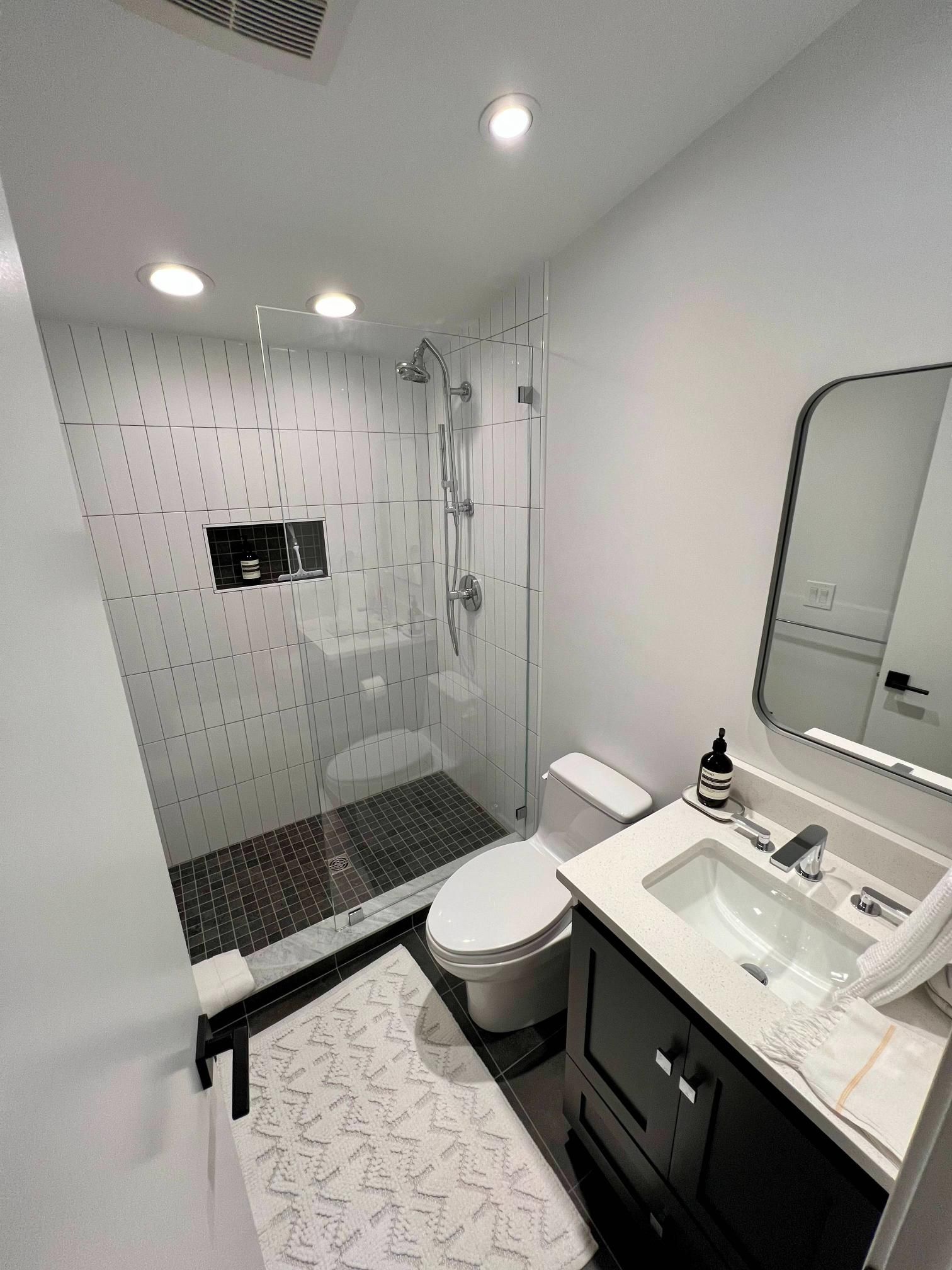 Modern white bathroom with glass shower, black vanity, and patterned floor tiles
