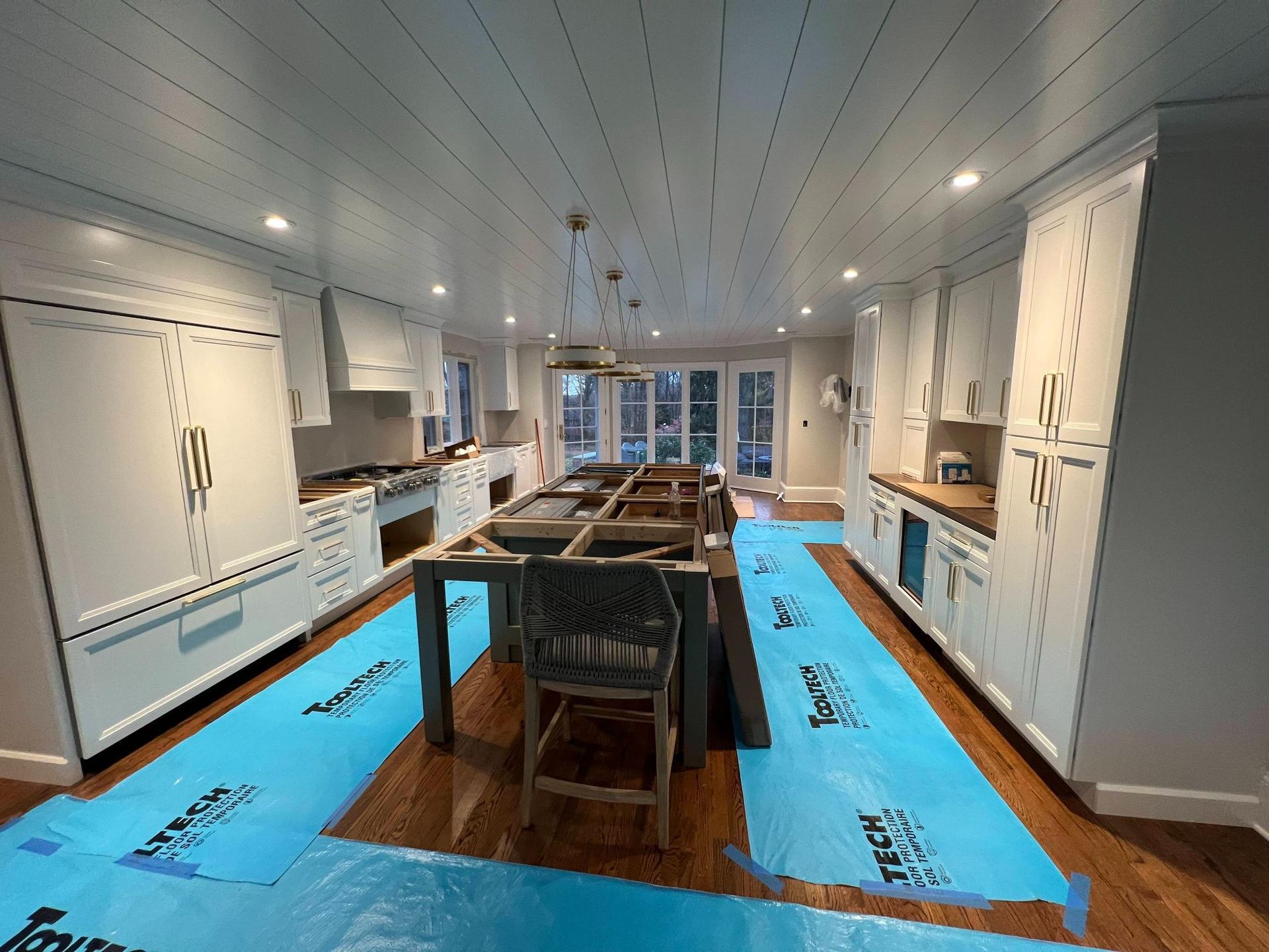 Bright modern kitchen under renovation, with blue floor protection and an island in the center.