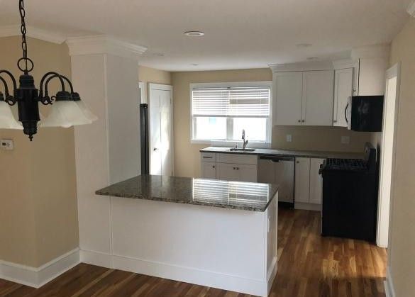 Bright kitchen with white cabinets, dark countertops, and wood floors, viewed from the dining area