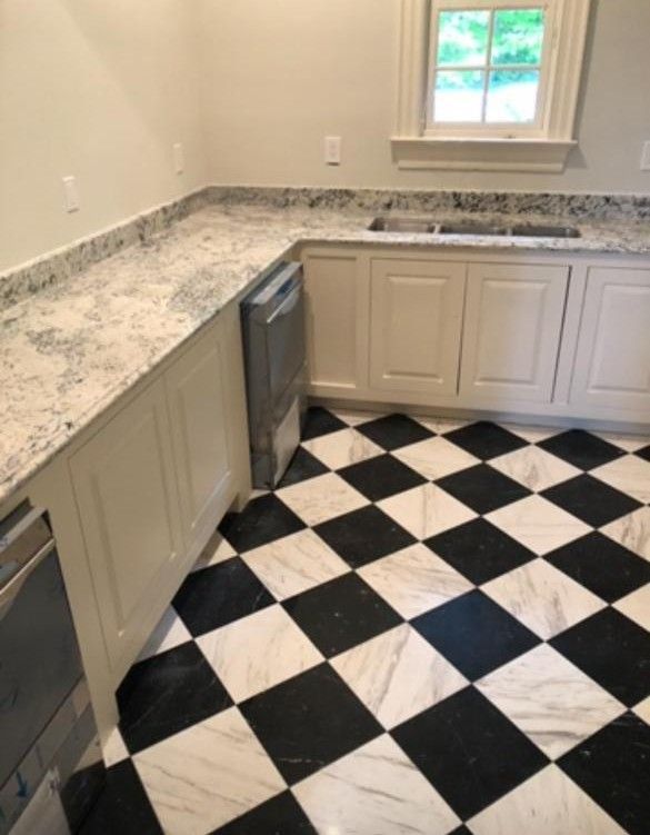 Small kitchen with black-and-white checkered floor, light cabinets, granite counters, and a window.