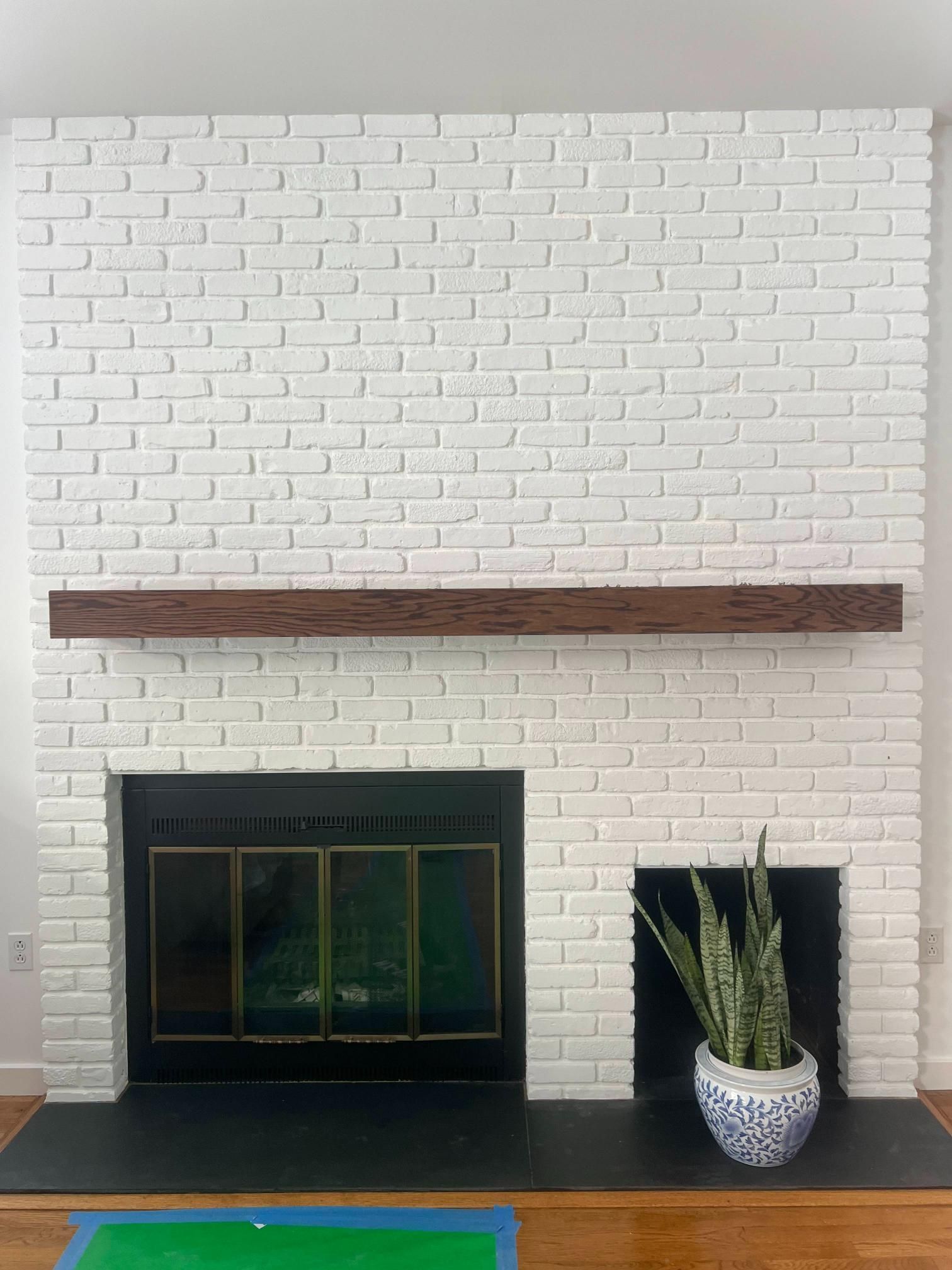 White brick fireplace with dark mantel, black firebox, and potted plant on the hearth.