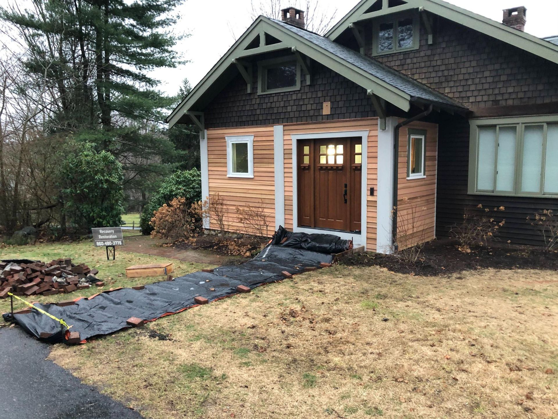 Front porch with lit double doors and a black walkway leading through a lawn beside a house.