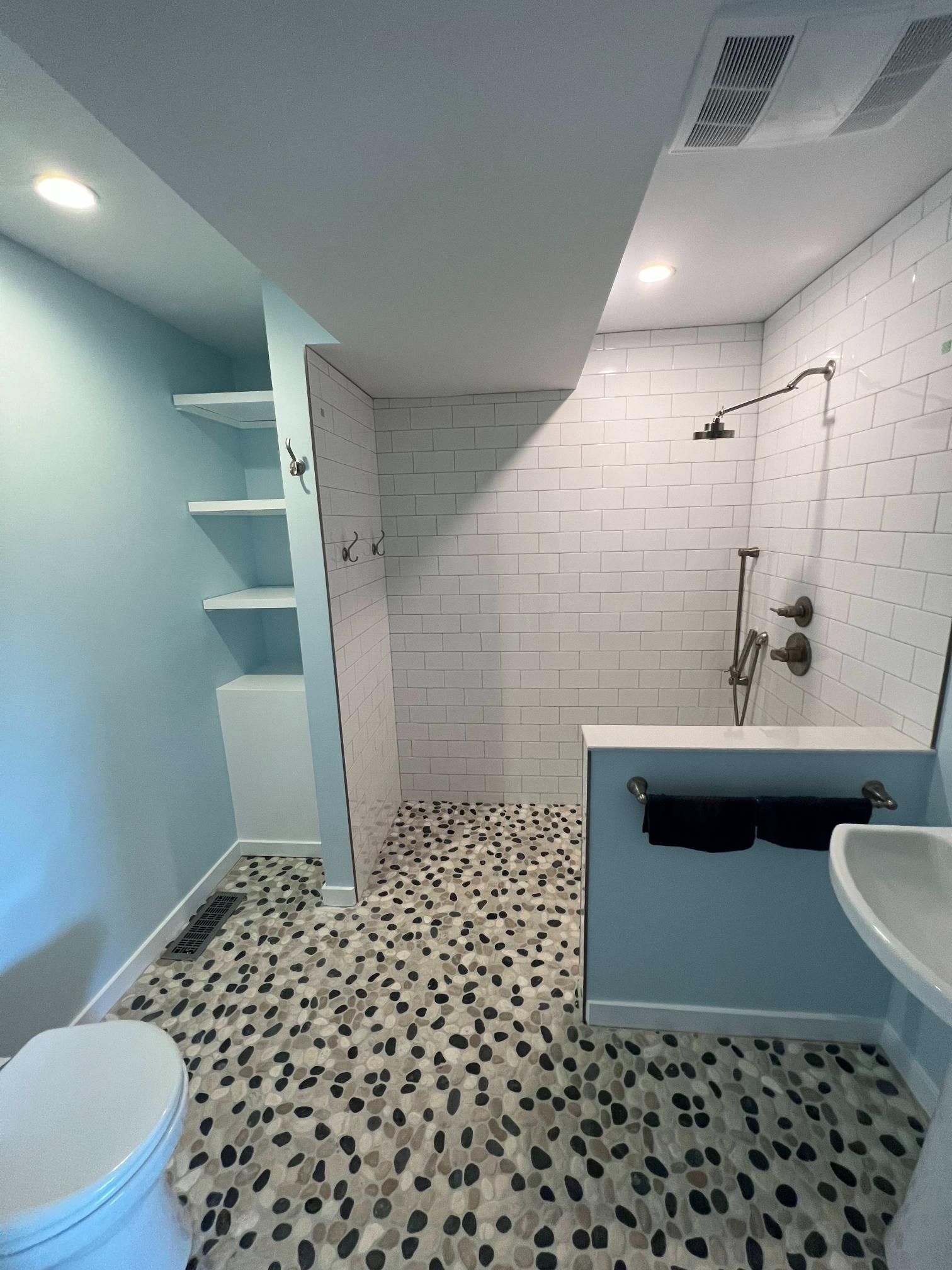 Modern bathroom with blue walls, tiled shower, pebble floor, sink, toilet, and built-in shelves