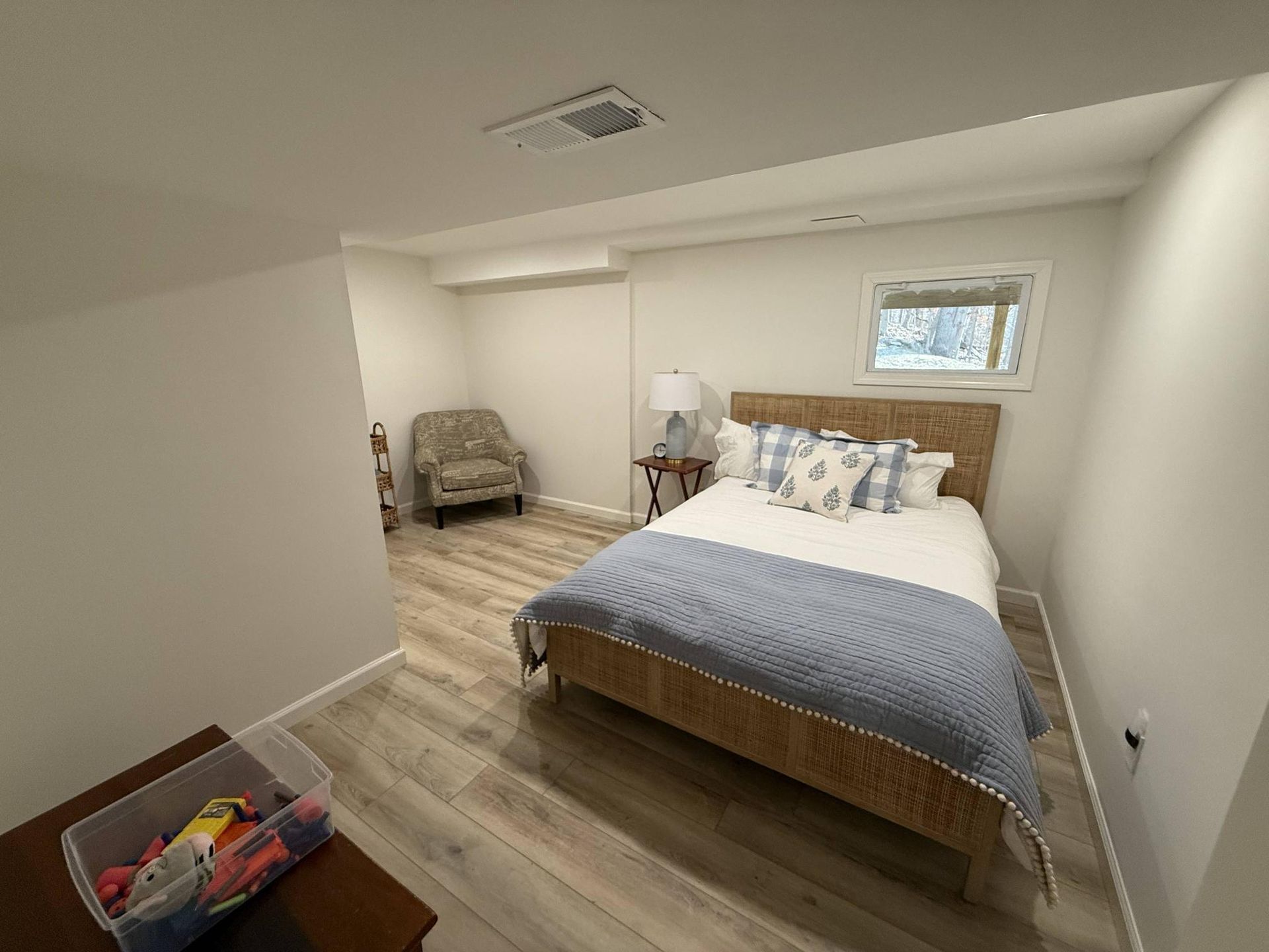 Bedroom with a bed, chair, lamp, and small window in a neutral-toned room.