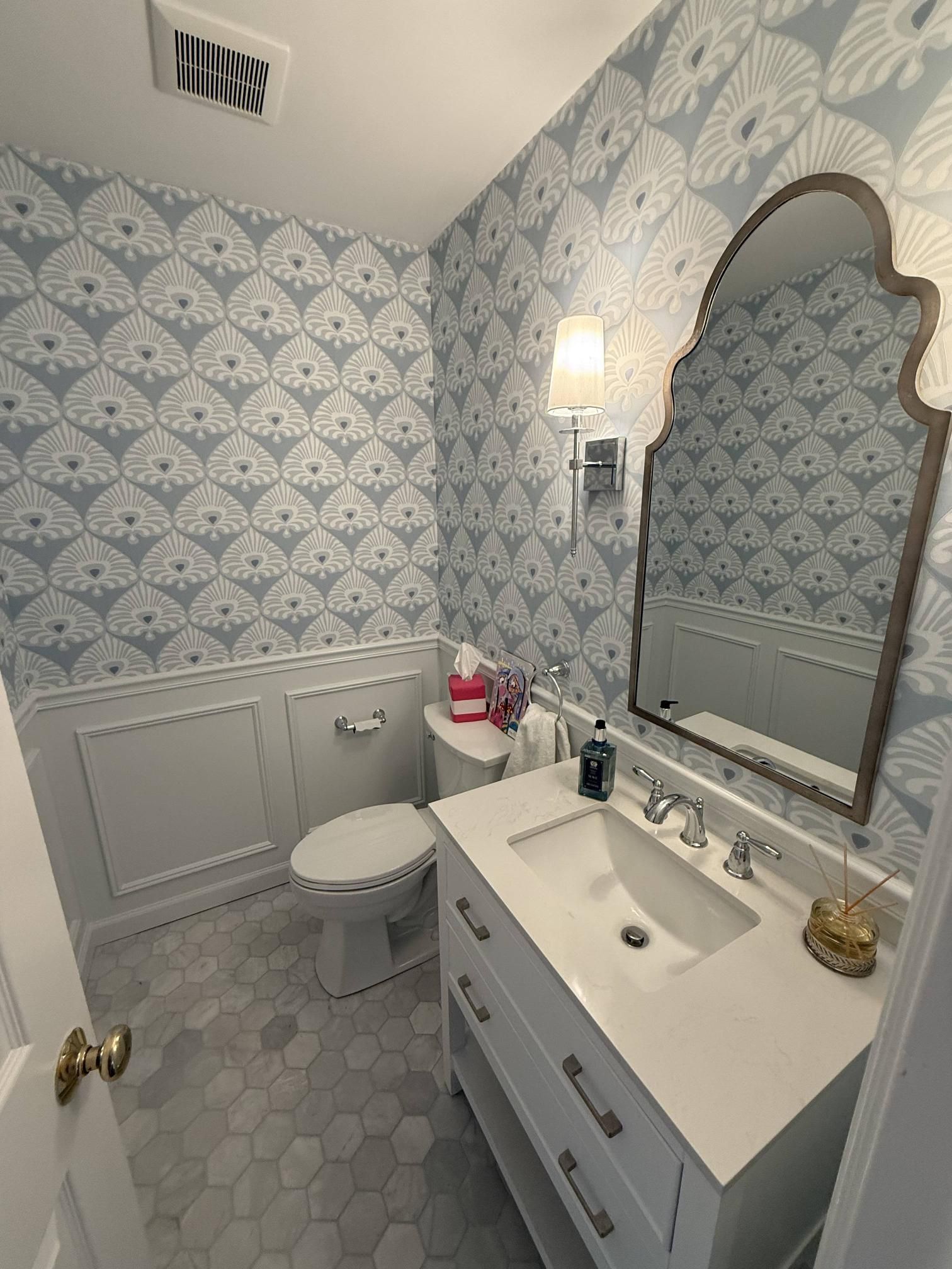 Small blue-and-white bathroom with toilet, sink vanity, mirror, and patterned wallpaper