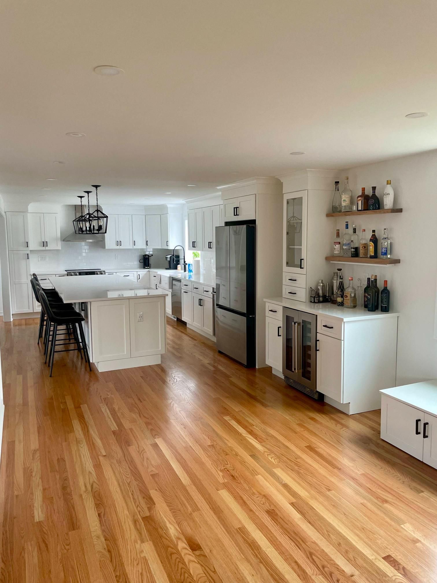 Bright open kitchen and living area with hardwood floors, white cabinets, island stools, and built-in shelves