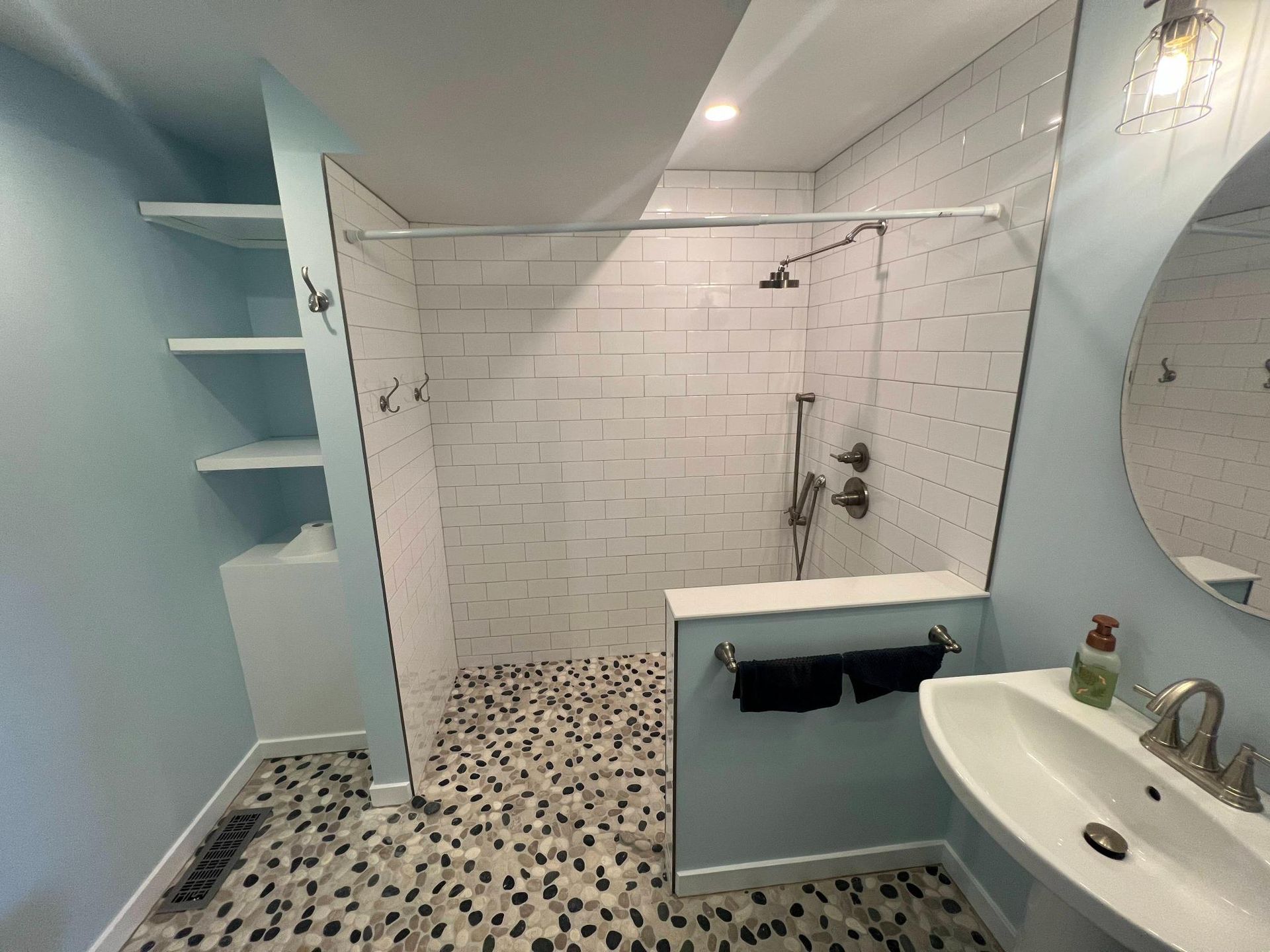 Modern bathroom with white subway-tile shower, blue walls, black-and-white floor, and round mirror