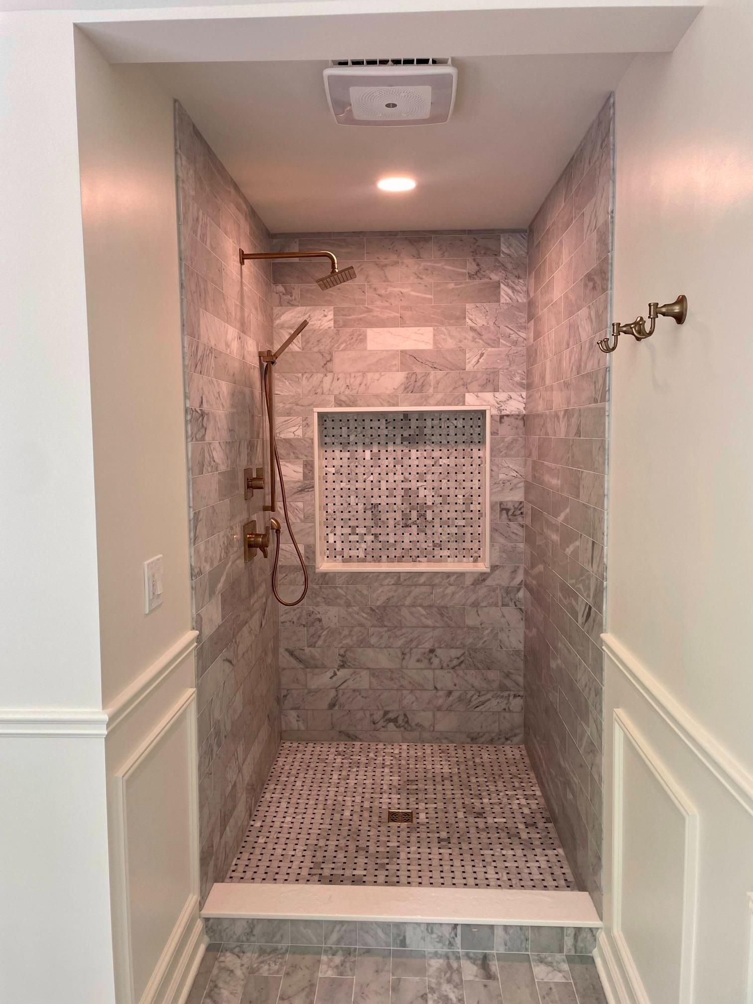 Accessible shower with grab bars, handheld showerhead, tiled floor, and built-in shower bench in a narrow stall