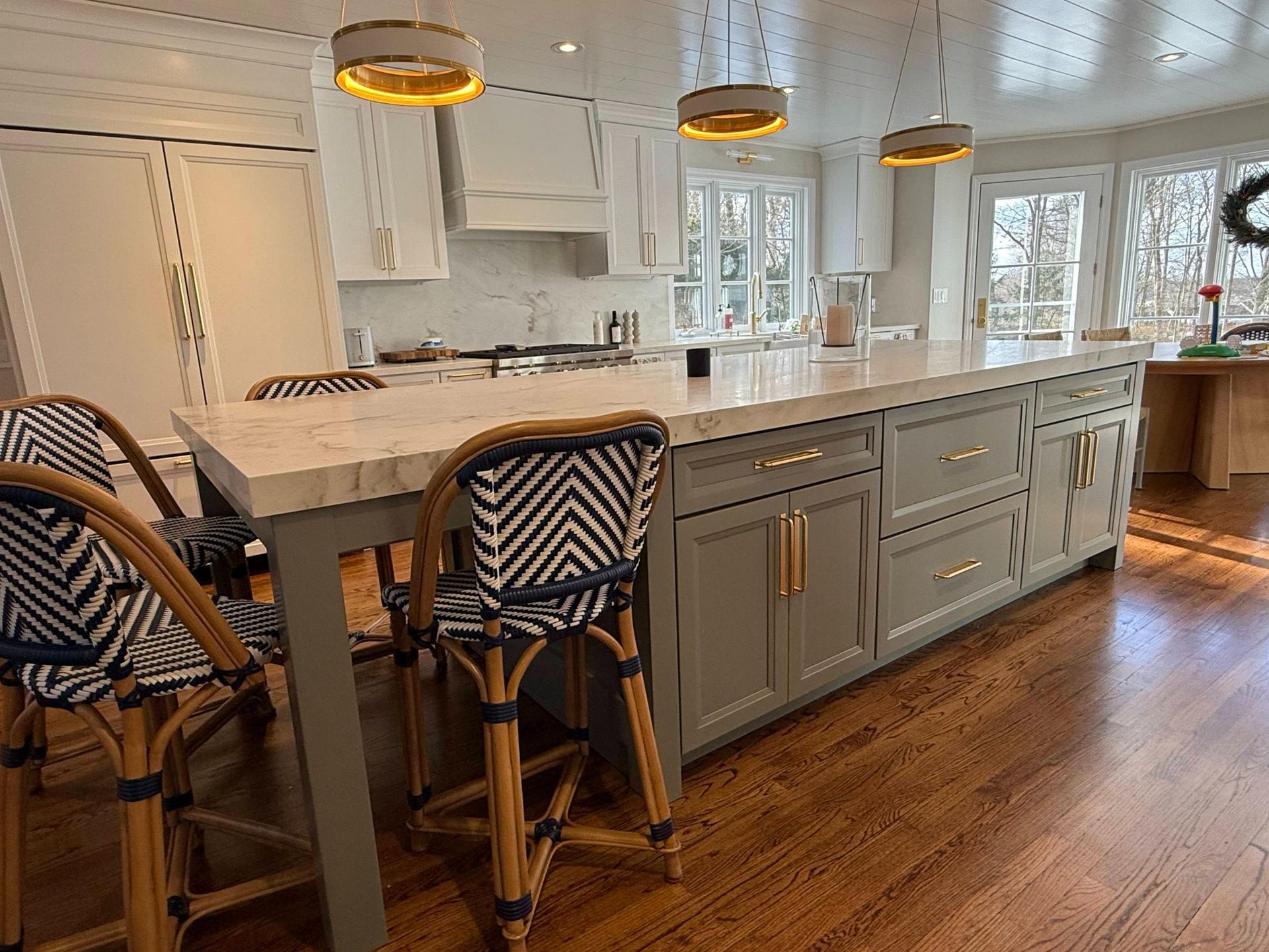 Modern white kitchen with large island, pendant lights, gray cabinets, and hardwood floors