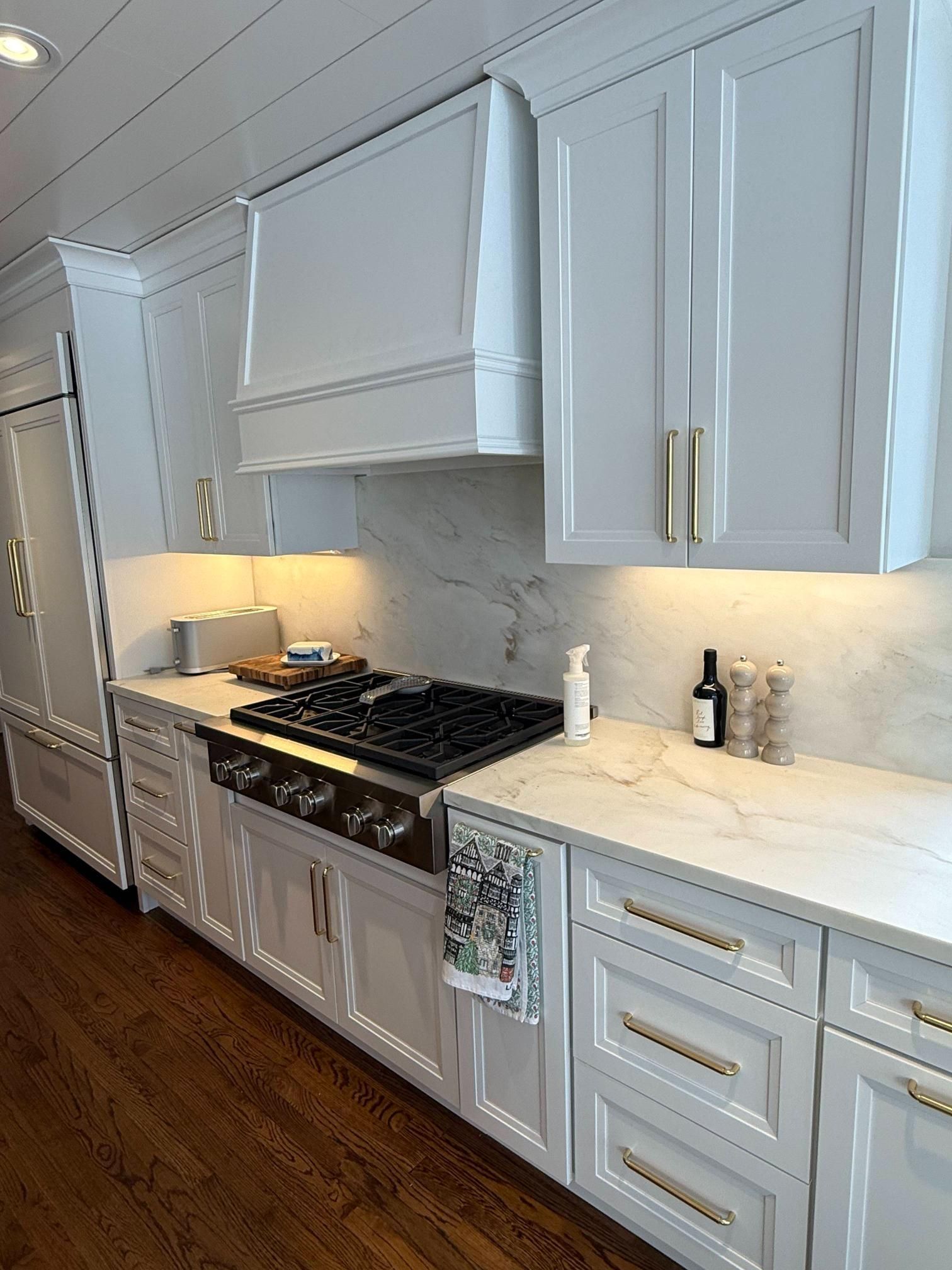 Modern white kitchen with marble countertops, stainless range, and hardwood floor