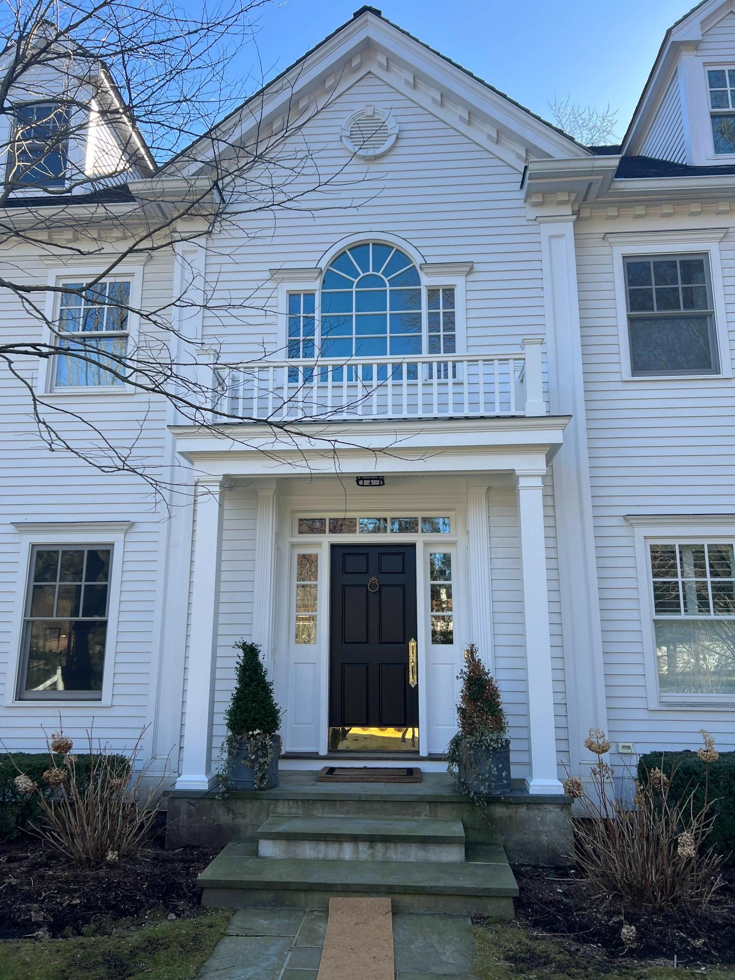 White two-story house with front porch, steps, and black front door under a blue sky
