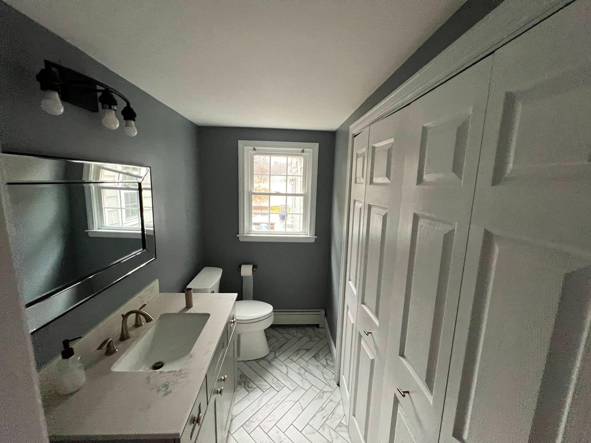 Modern gray bathroom with double vanity, toilet, and shower door near a window.