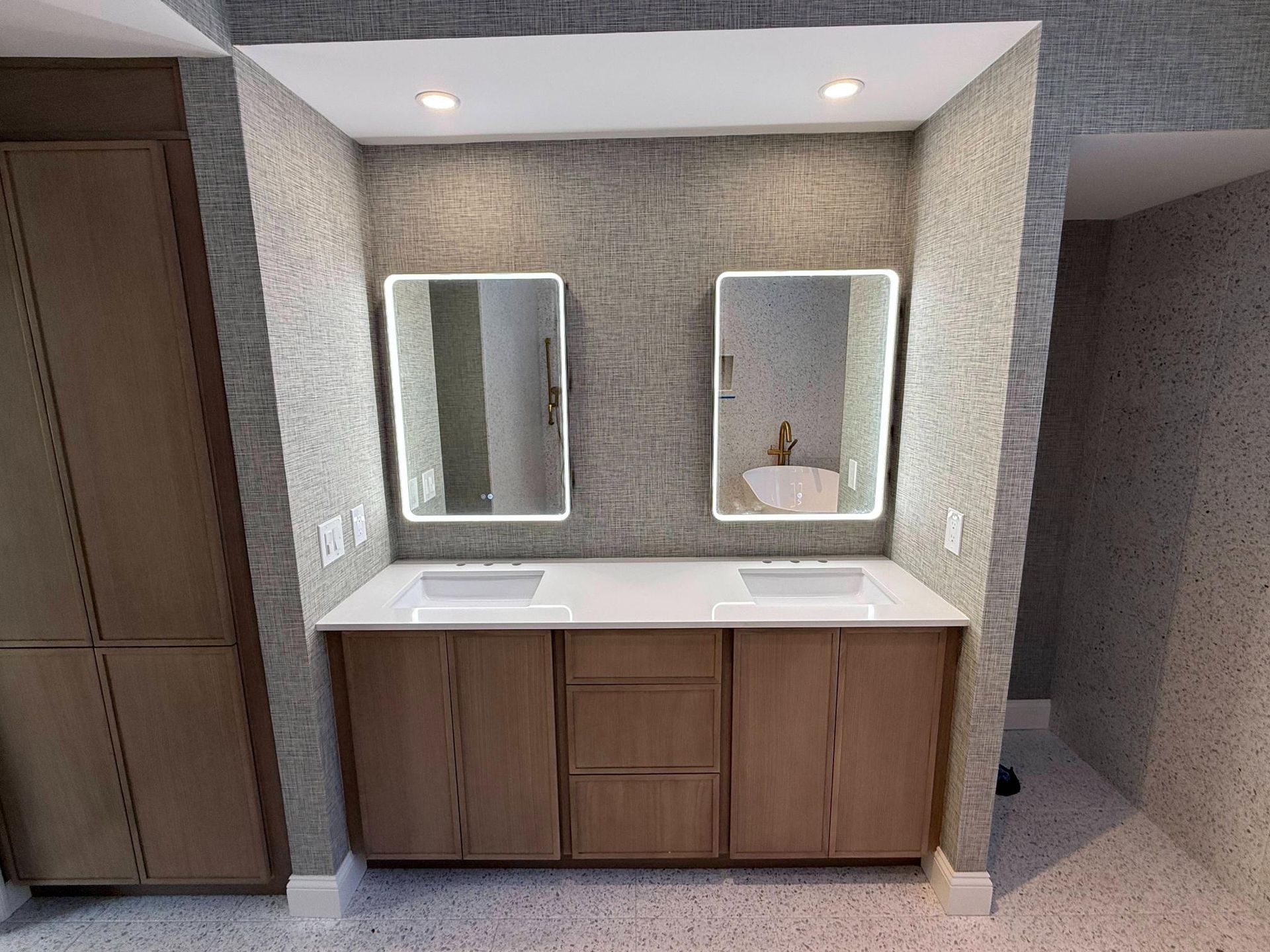 Modern bathroom vanity with double sinks, mirrors, and wood cabinetry beneath a lit recessed alcove.
