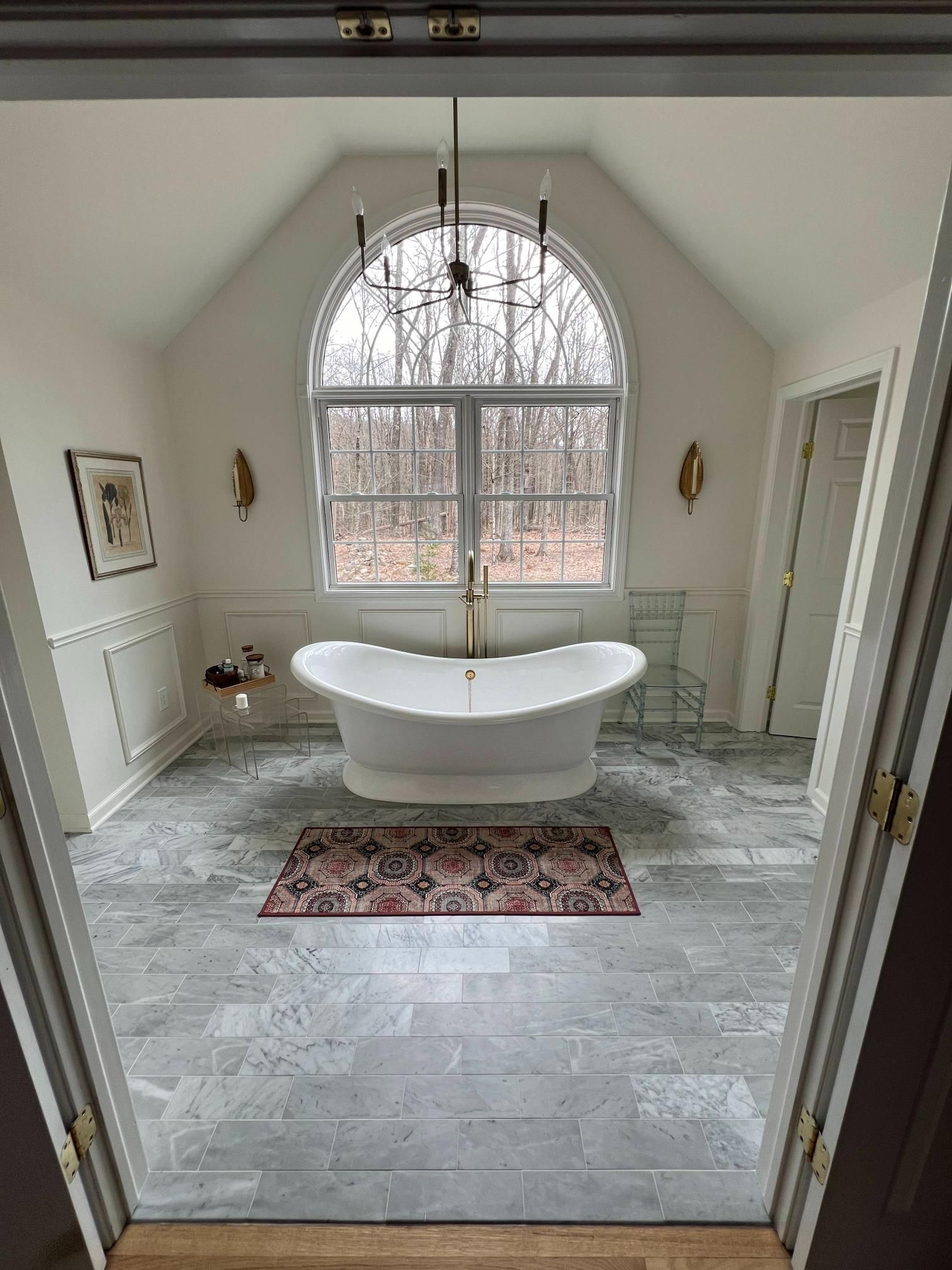 Bright bathroom with a freestanding tub before an arched window and gray tile floor