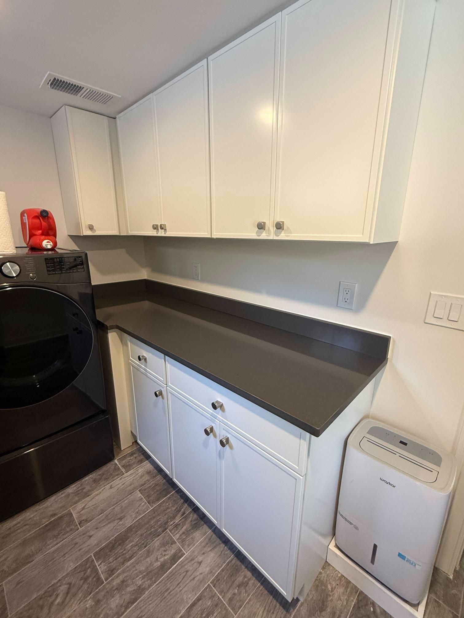 Laundry room with white cabinets, dark countertop, washer and dryer, and gray tile floor