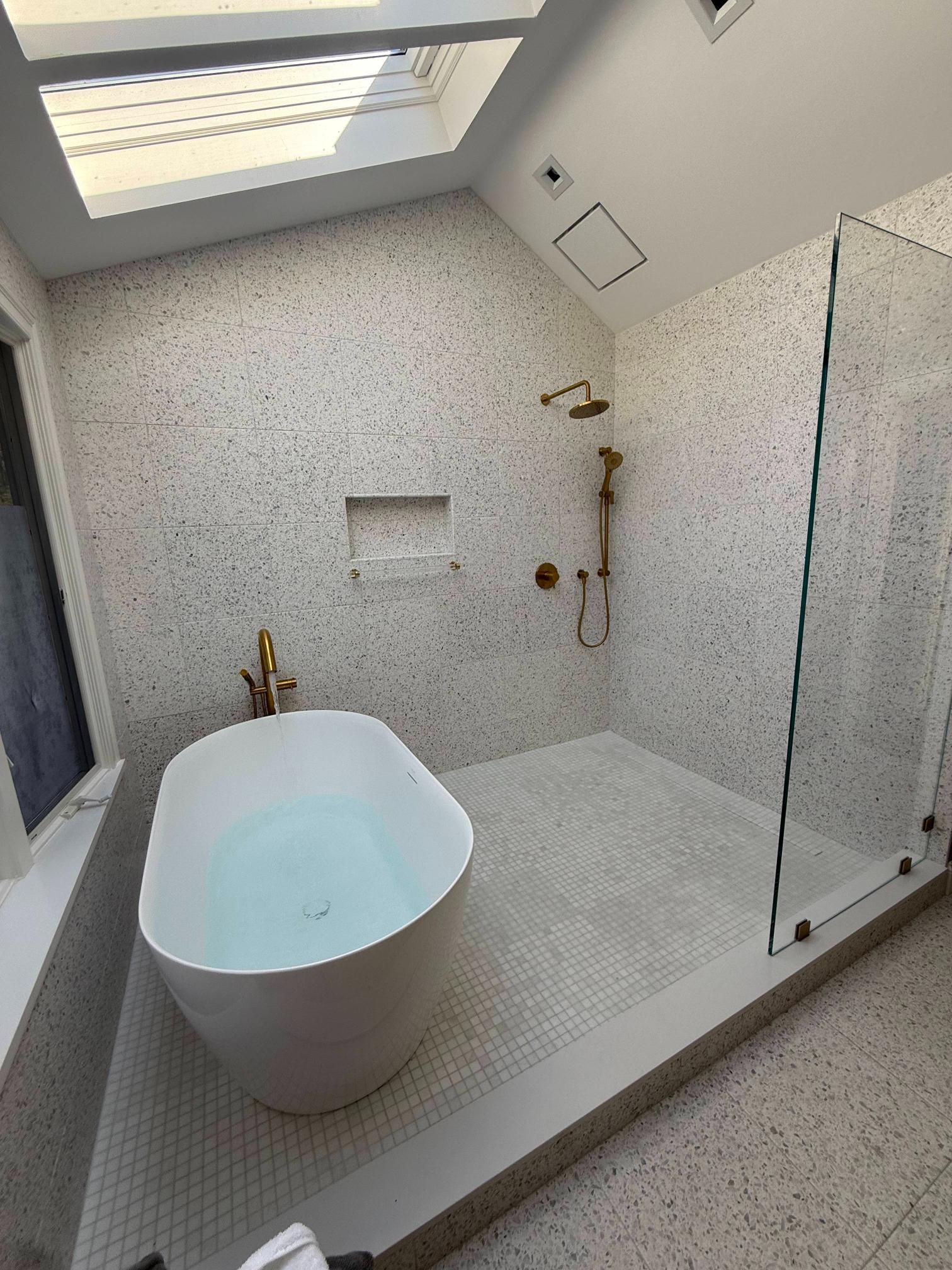 Modern bathroom with freestanding tub, glass shower, skylight, and mosaic tile walls and floor