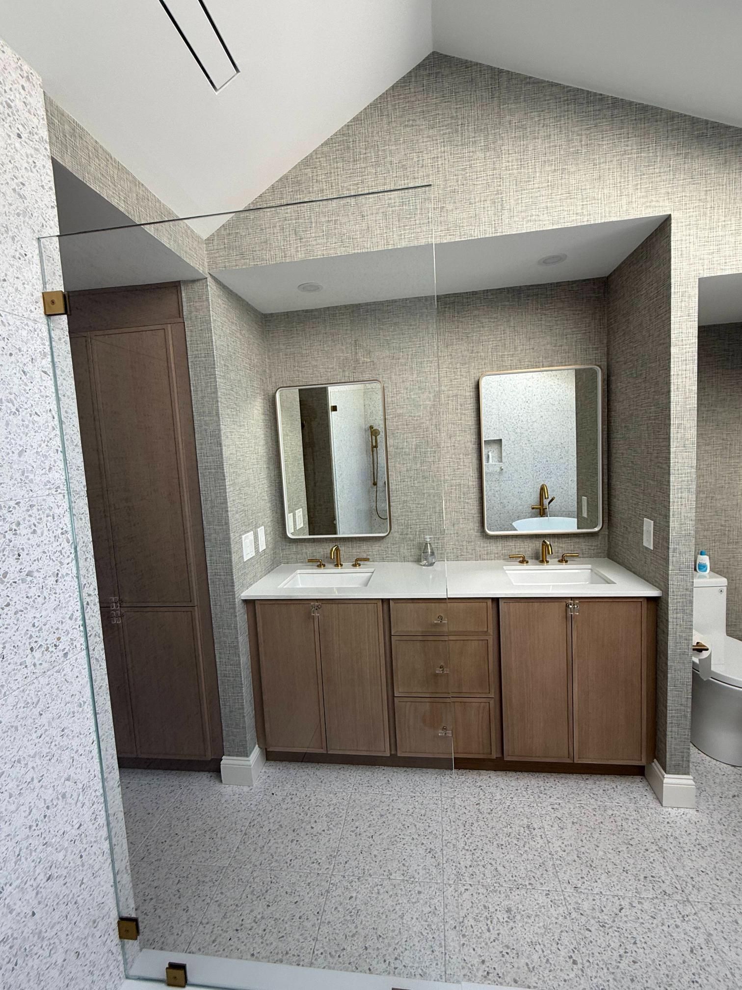 Small bathroom vanity with two mirrors, wood cabinets, white countertop, and tiled walls and floor.