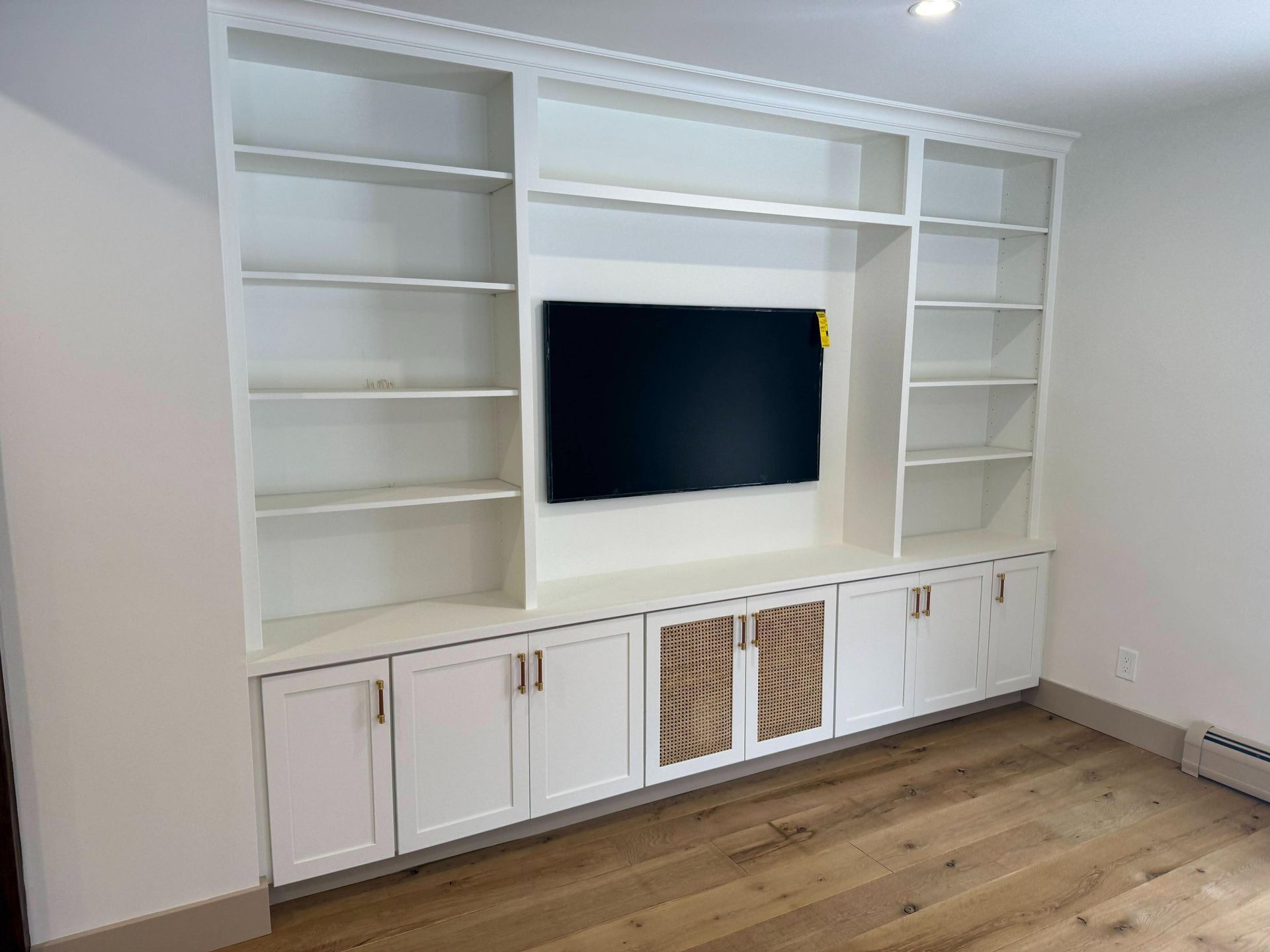 White built-in TV cabinet with shelves and cabinets against a wall in a room with wood flooring.