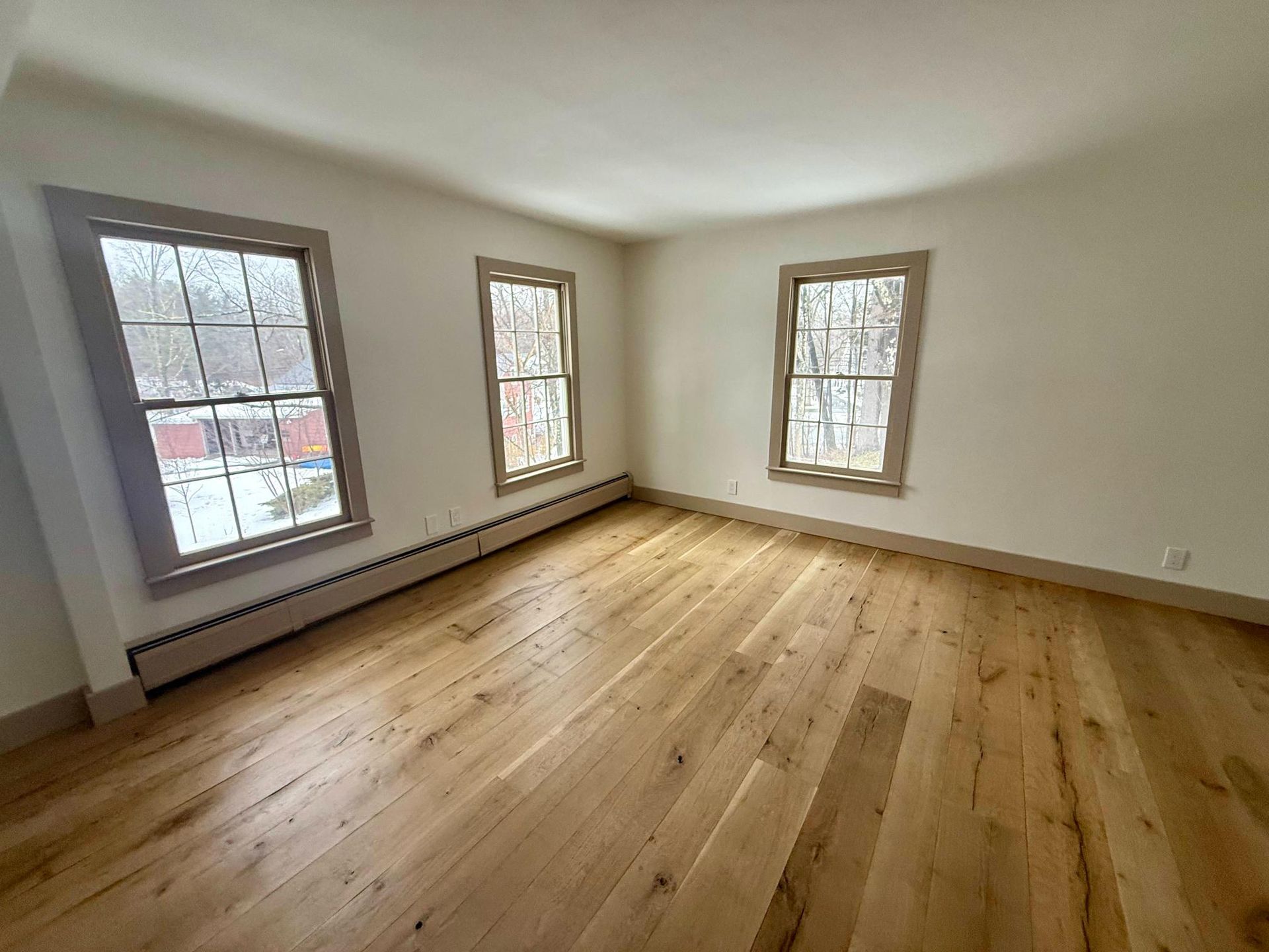 Empty room with hardwood floors and three windows letting in daylight