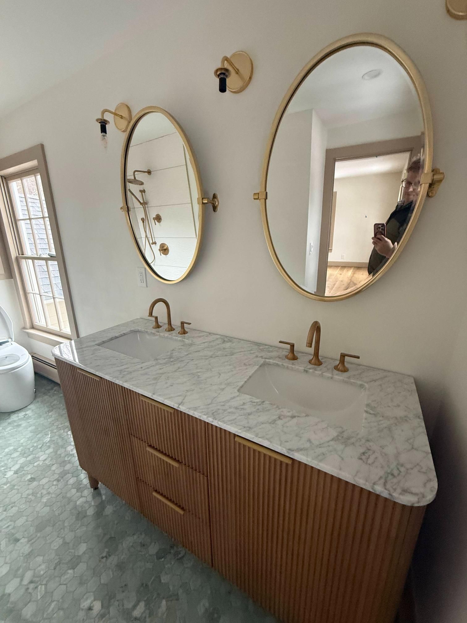 Modern bathroom vanity with two gold oval mirrors, double sinks, and marble countertop