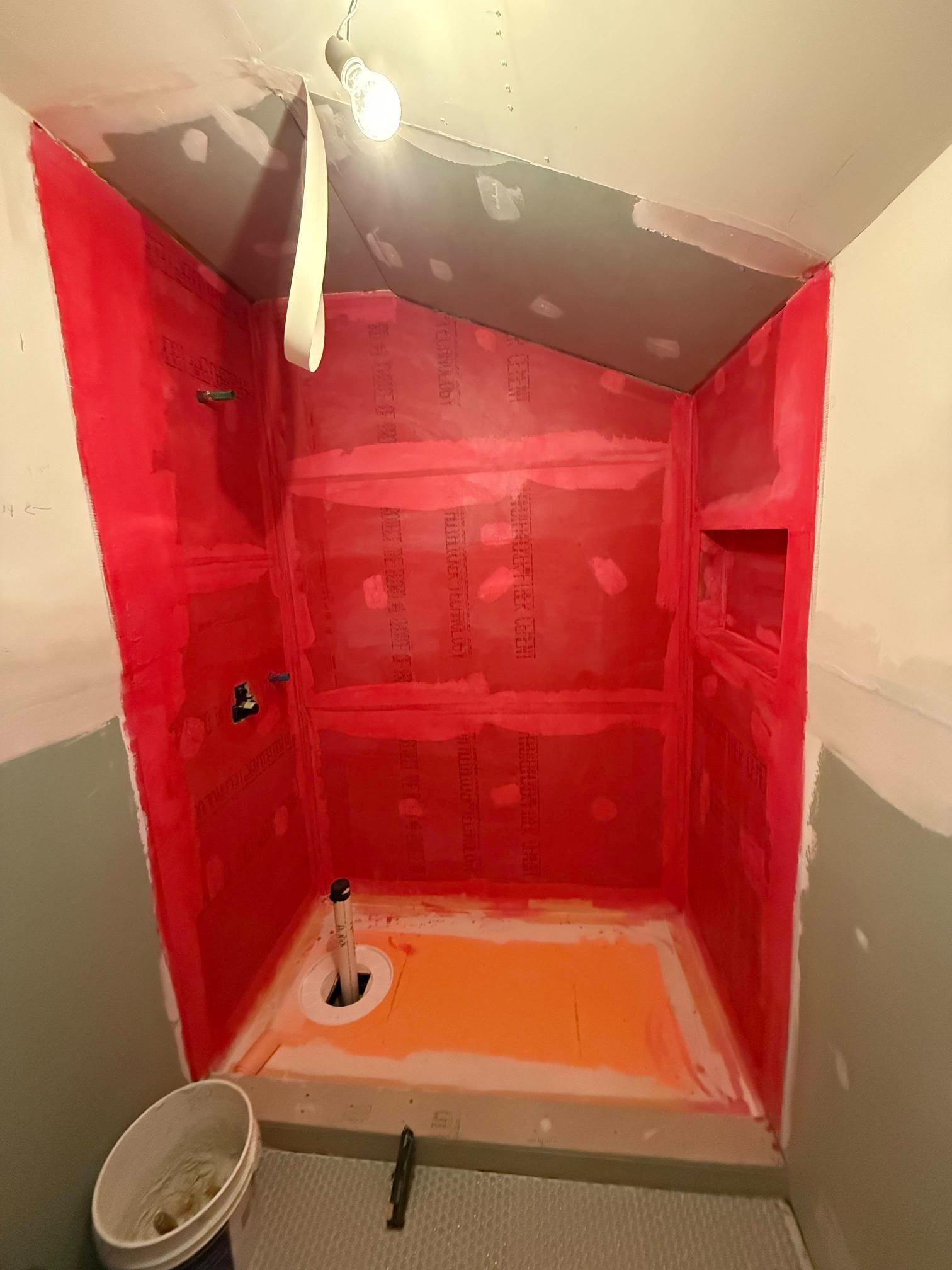 Red-tiled shower alcove under renovation, with exposed walls, orange floor, and a showerhead overhead