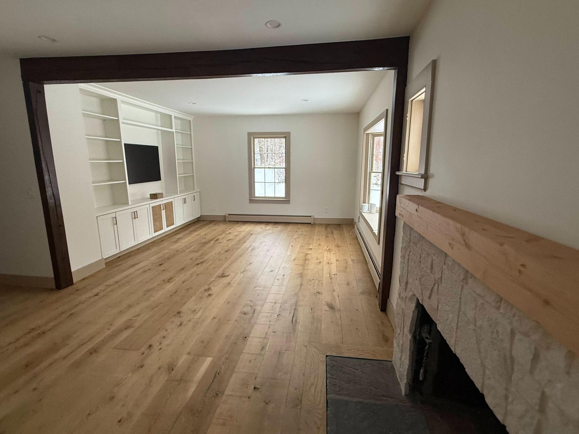 Empty living room with hardwood floors, white built-in shelving, a fireplace, and windows bringing in natural light