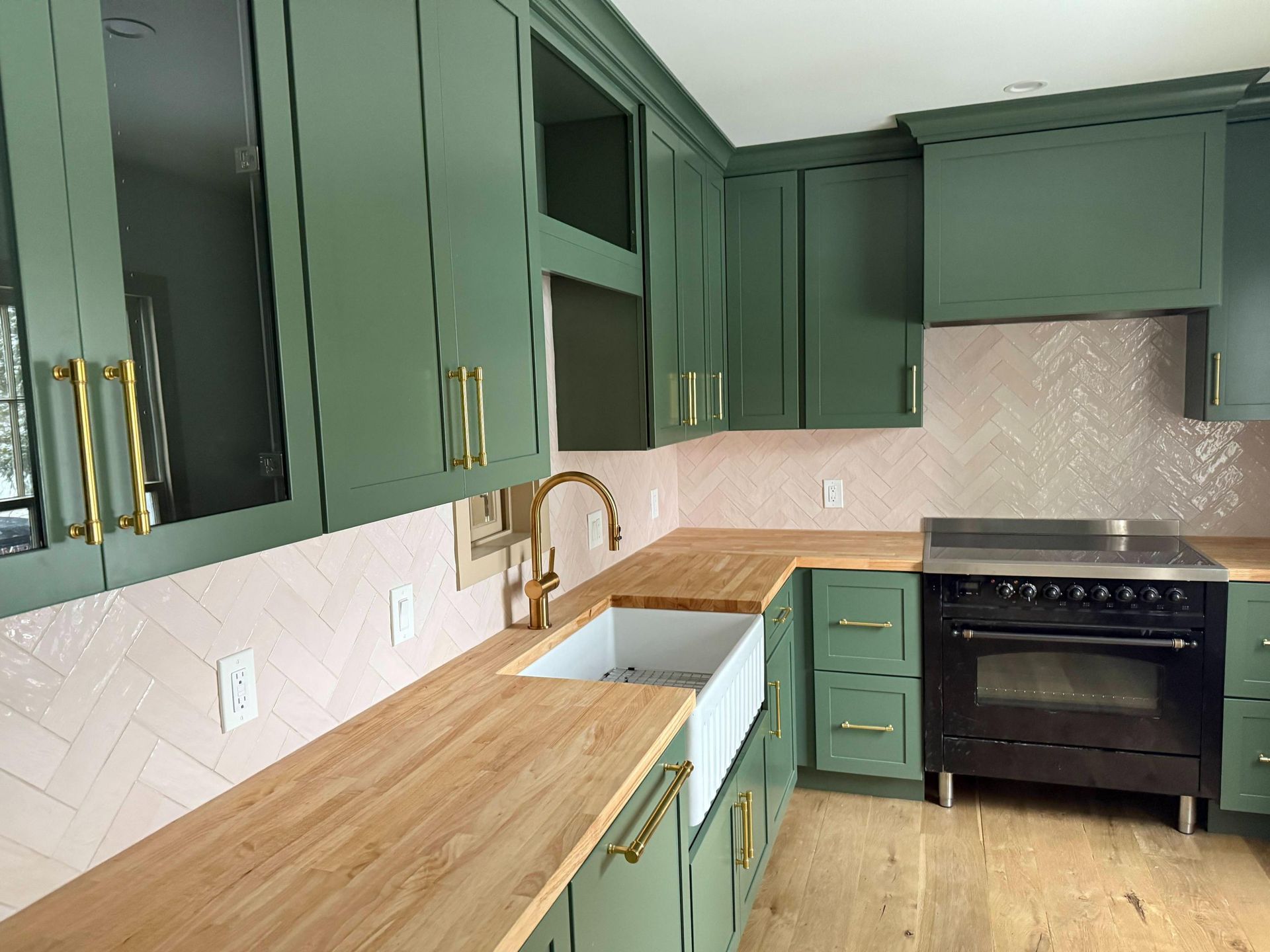 Dark green kitchen cabinets with wood countertops, white tile backsplash, sink, and black stove.