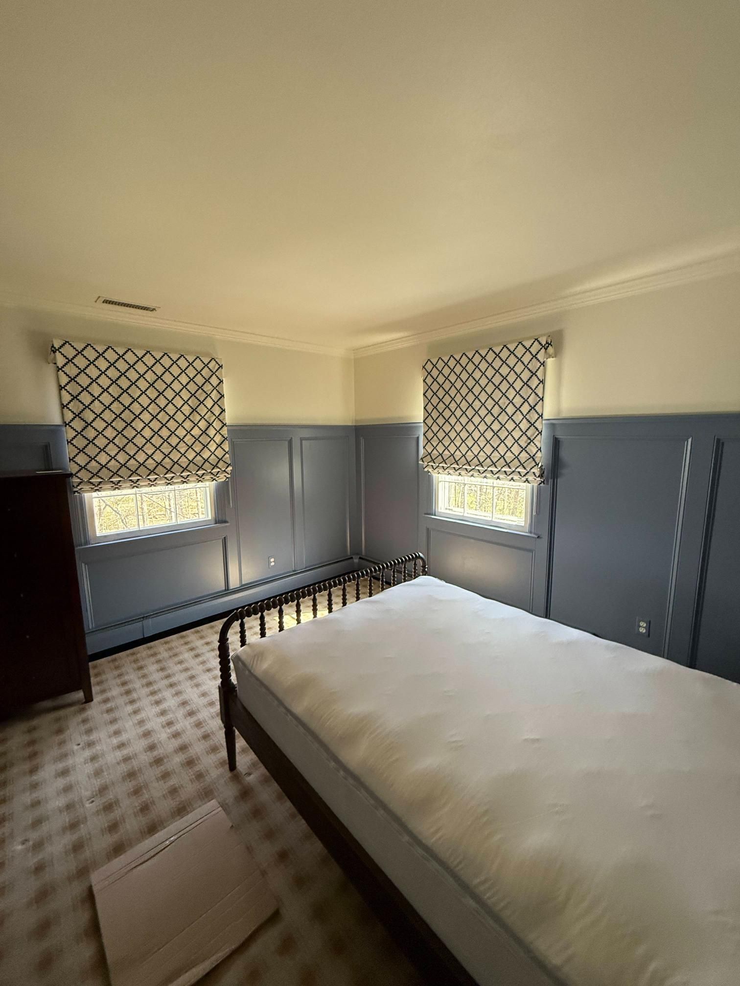 Small bedroom with blue paneled walls, patterned blinds, and a bed in the foreground.
