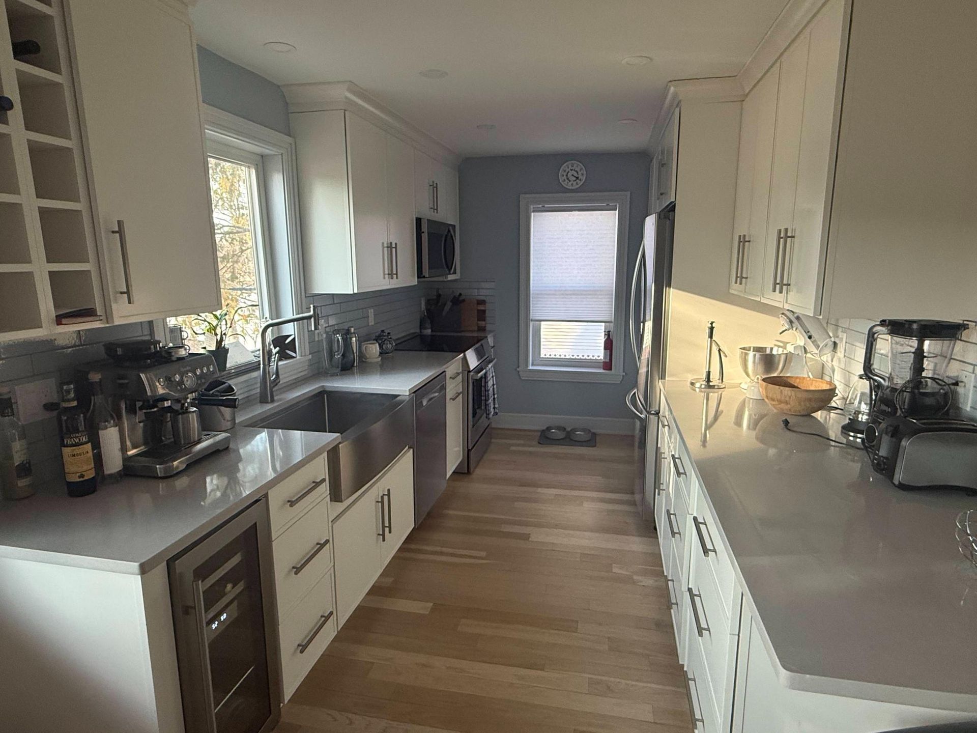 Bright galley kitchen with white cabinets, gray countertops, and wood flooring.