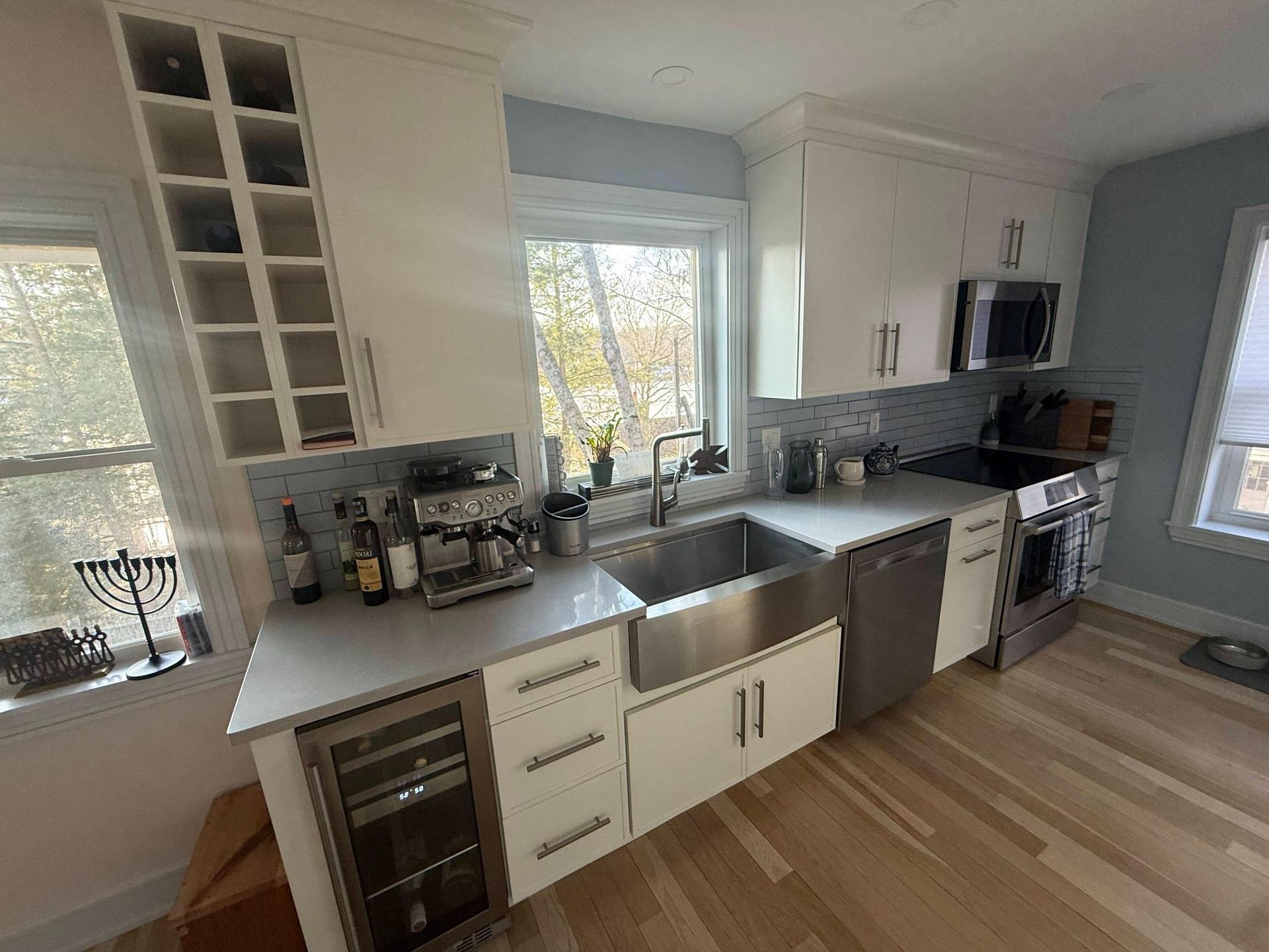 Bright modern kitchen with white cabinets, stainless sink, gray countertop, and wood floor
