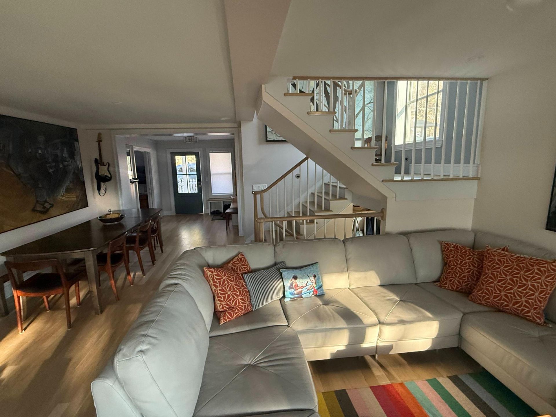 Bright living room with beige sectional, dining table, and staircase leading to an upper floor.