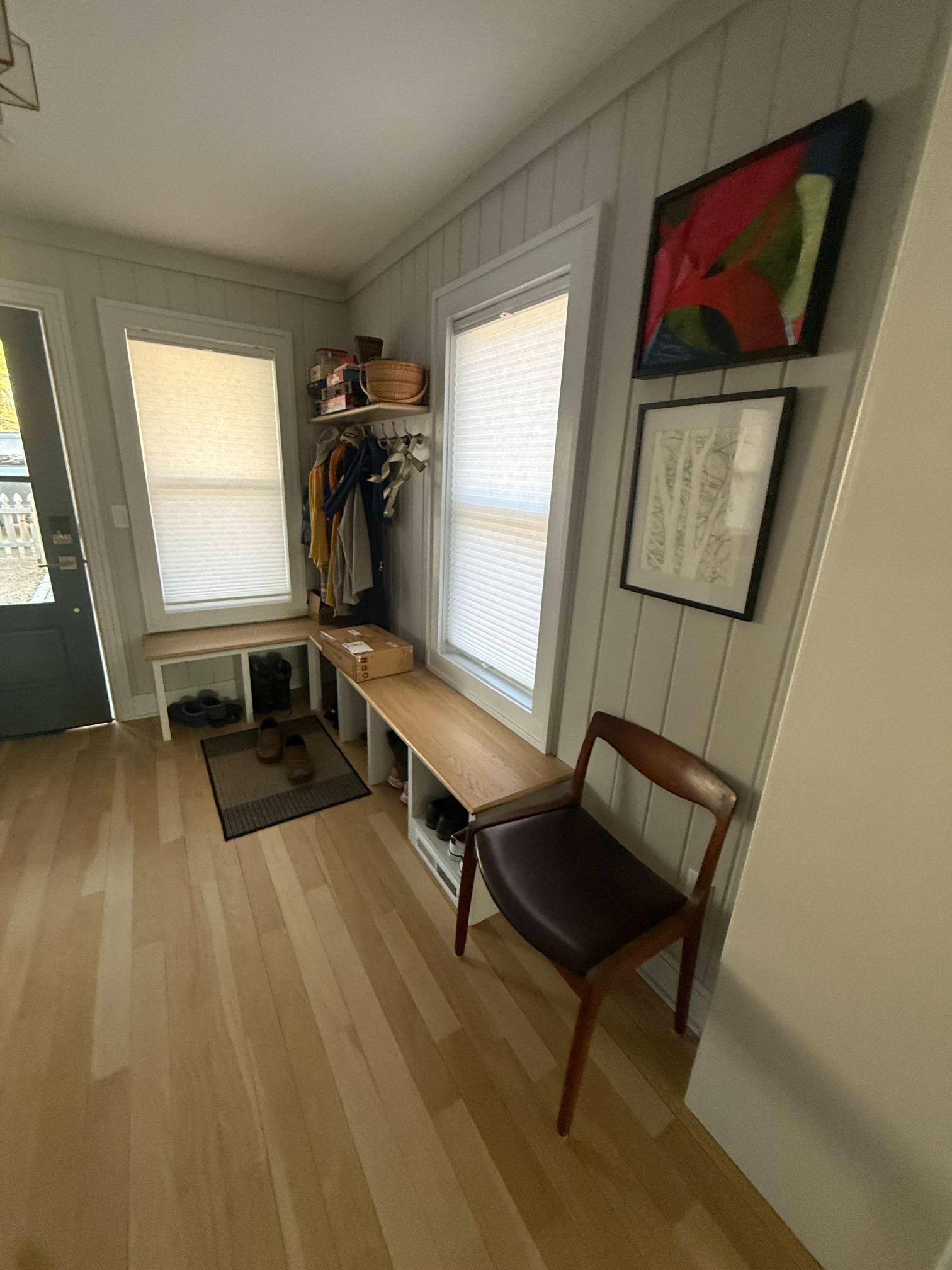 Narrow entryway with bench, coat rack, artwork, and two windows with blinds.
