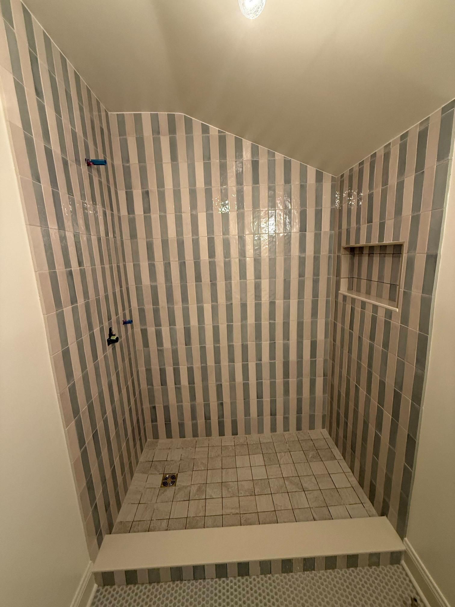 Striped-tile shower stall with recessed shelf and showerhead mount, viewed from the entrance.