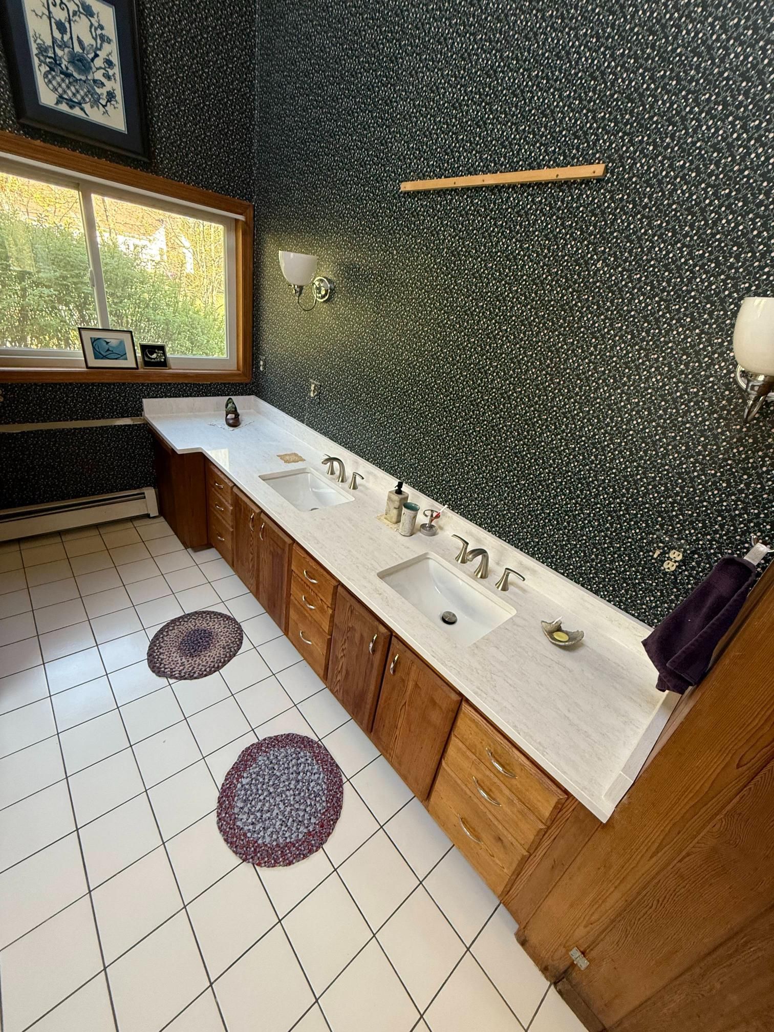 Modern restroom with long white sink counter, wood cabinets, tiled floor, and speckled green walls.