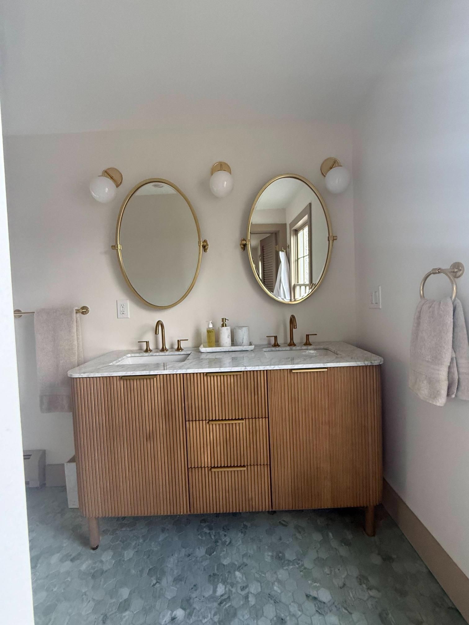 Modern bathroom vanity with wood cabinets, two oval mirrors, and white sink under wall sconces.