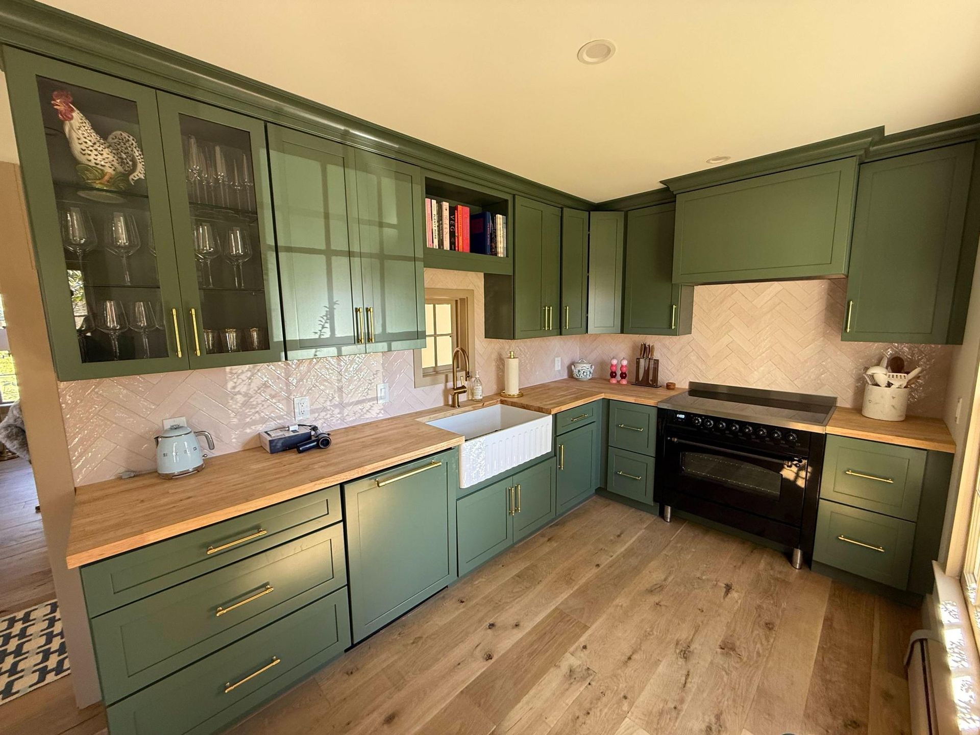 Green kitchen with wood countertops, black stove, white sink, and light wood floors