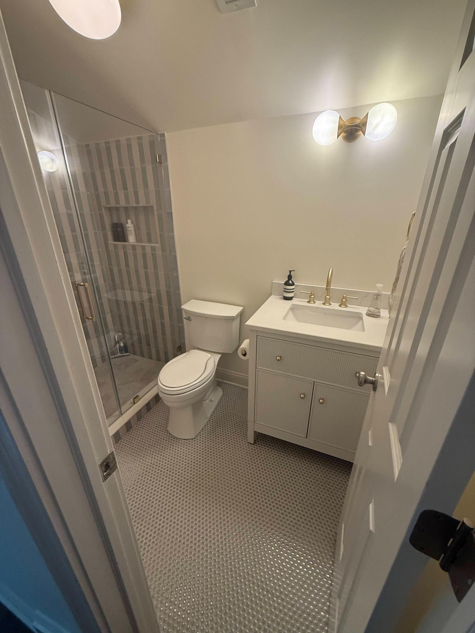 Small bathroom with toilet, sink vanity, shower stall, and patterned tile floor.