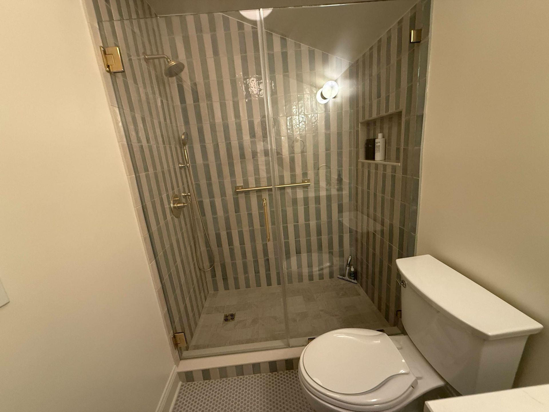 Small bathroom with a glass shower, toilet, beige walls, and striped shower curtain.