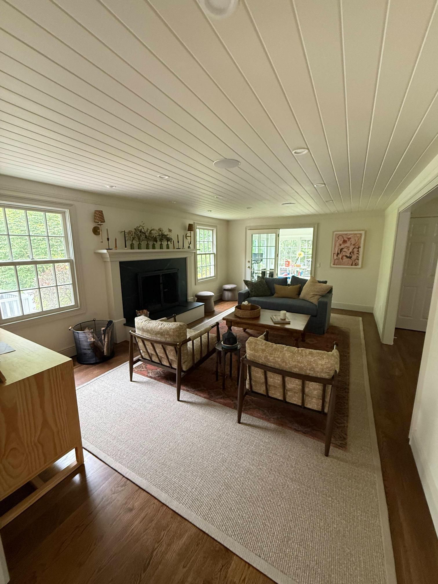Bright living room with white ceiling, hardwood floors, rug, sofas, chairs, fireplace, and large windows.