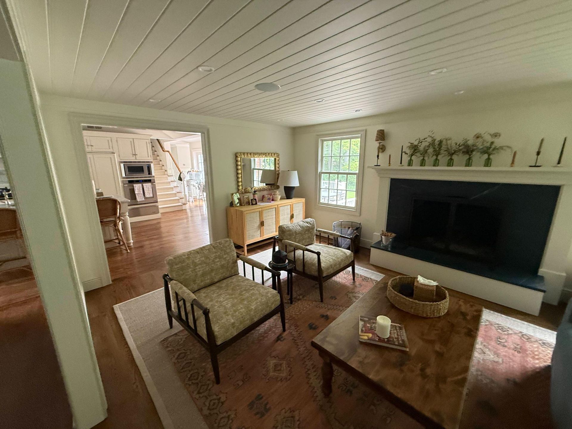 Bright living room with white walls, beige chairs, wood coffee table, large TV, and sunlit windows