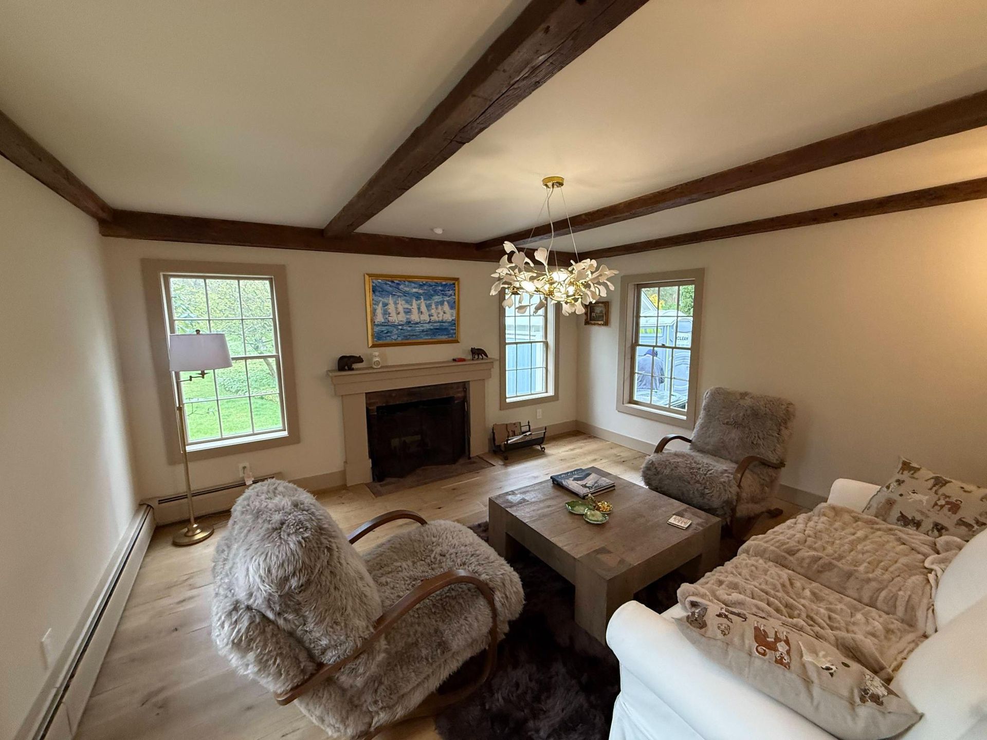Cozy living room with fireplace, large windows, exposed beams, and plush seating around a coffee table
