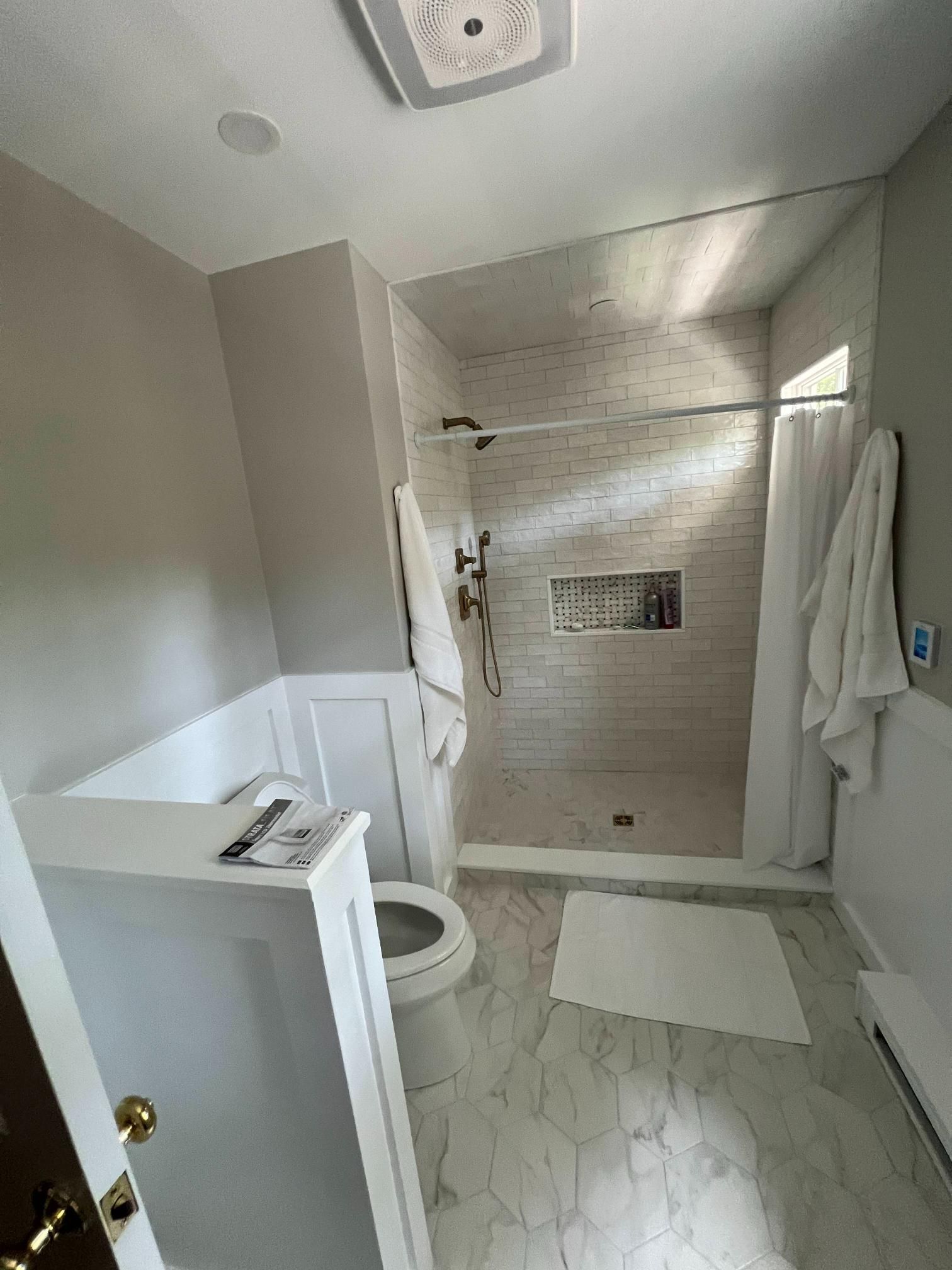 Small bathroom with walk-in tiled shower, toilet, vanity, and towels on a light floor.