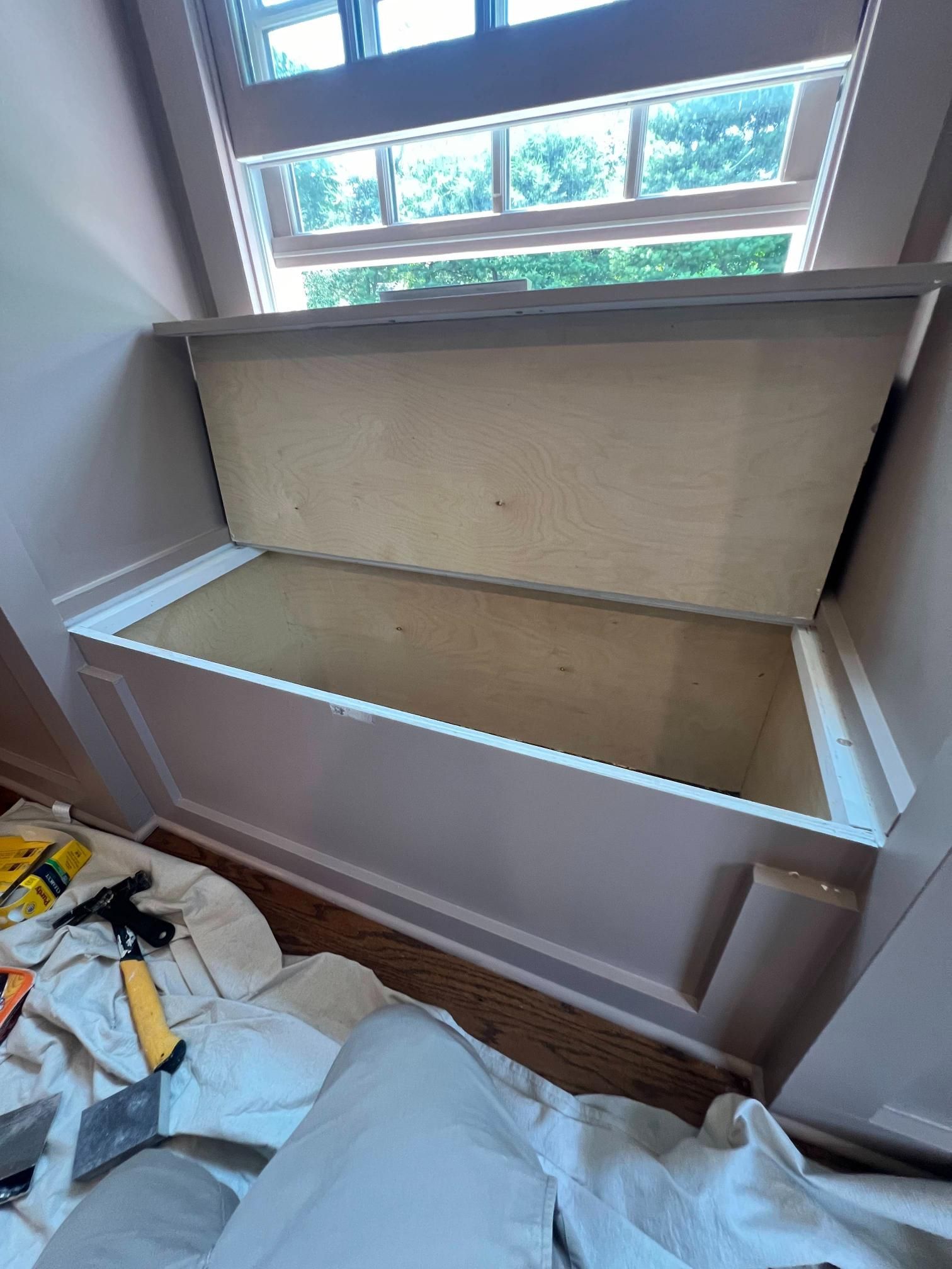 Open window seat storage bench under a skylight, with construction materials on the floor.