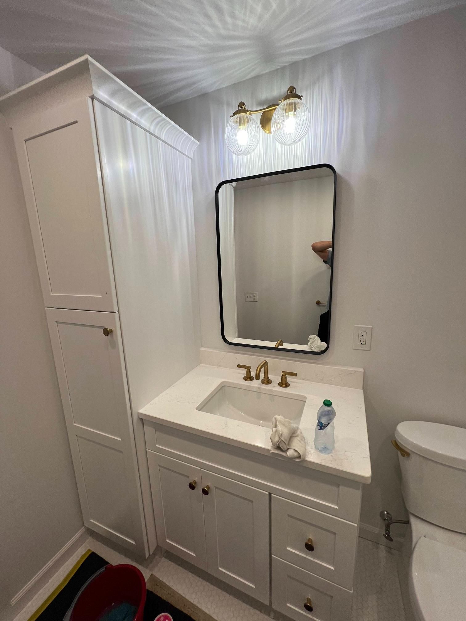 White bathroom vanity with mirror, brass light fixture, cabinet storage, and a toilet beside it
