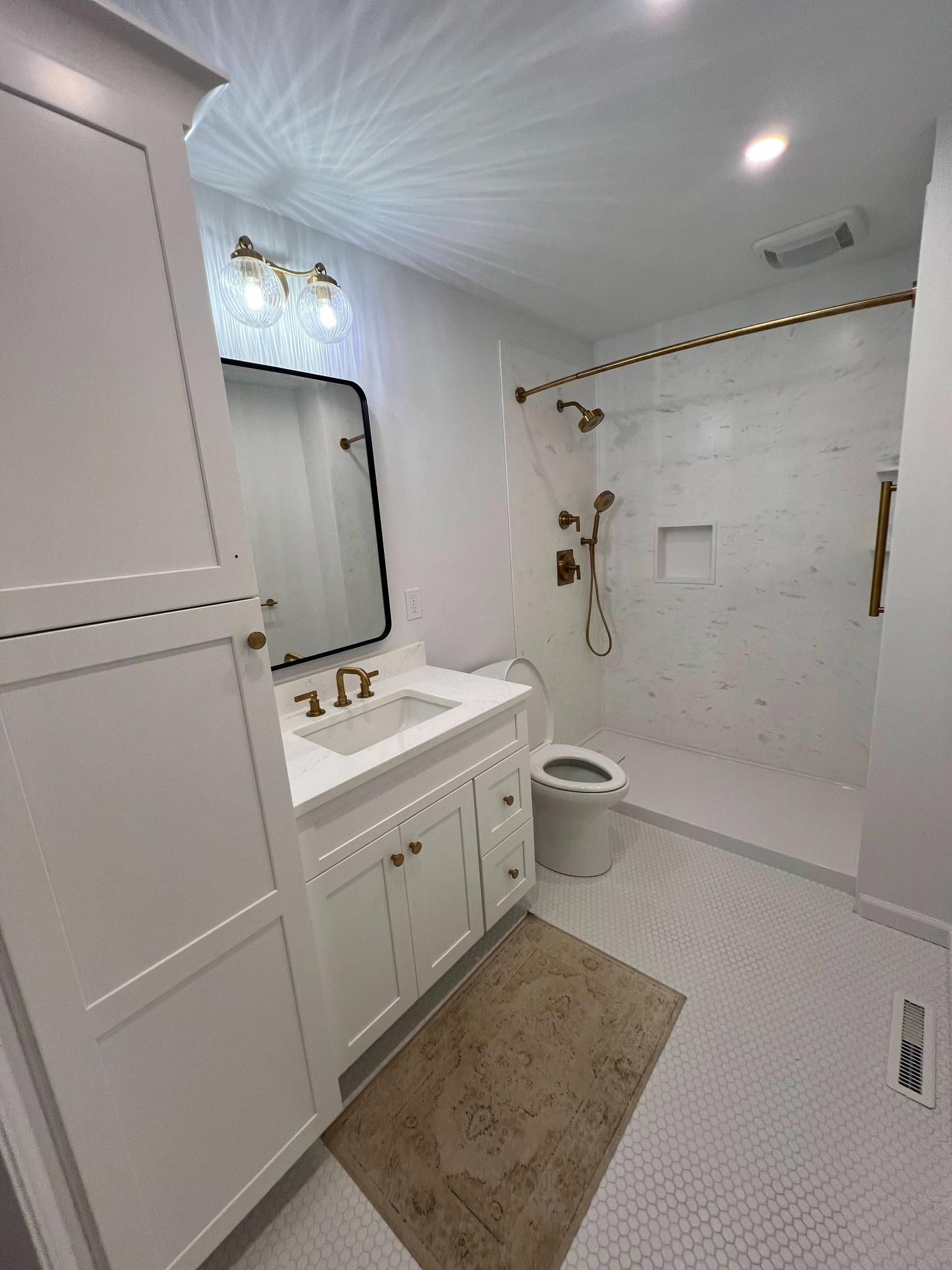 Bright white bathroom with vanity, mirror, toilet, shower, and beige rug